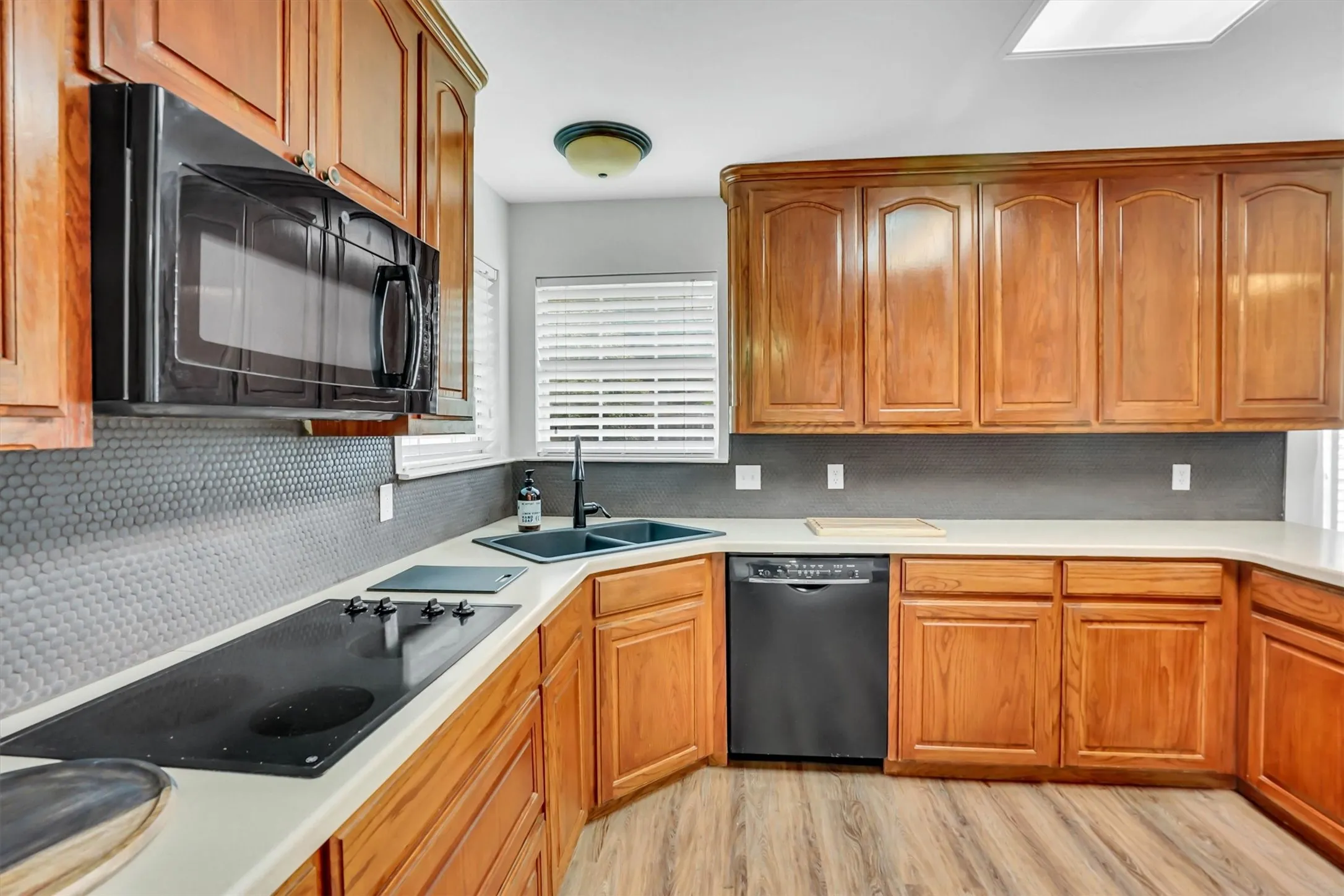 Kitchen featuring warm wood cabinetry, light countertops, a built-in cooktop, and a black double-basin sink with a matte black faucet
