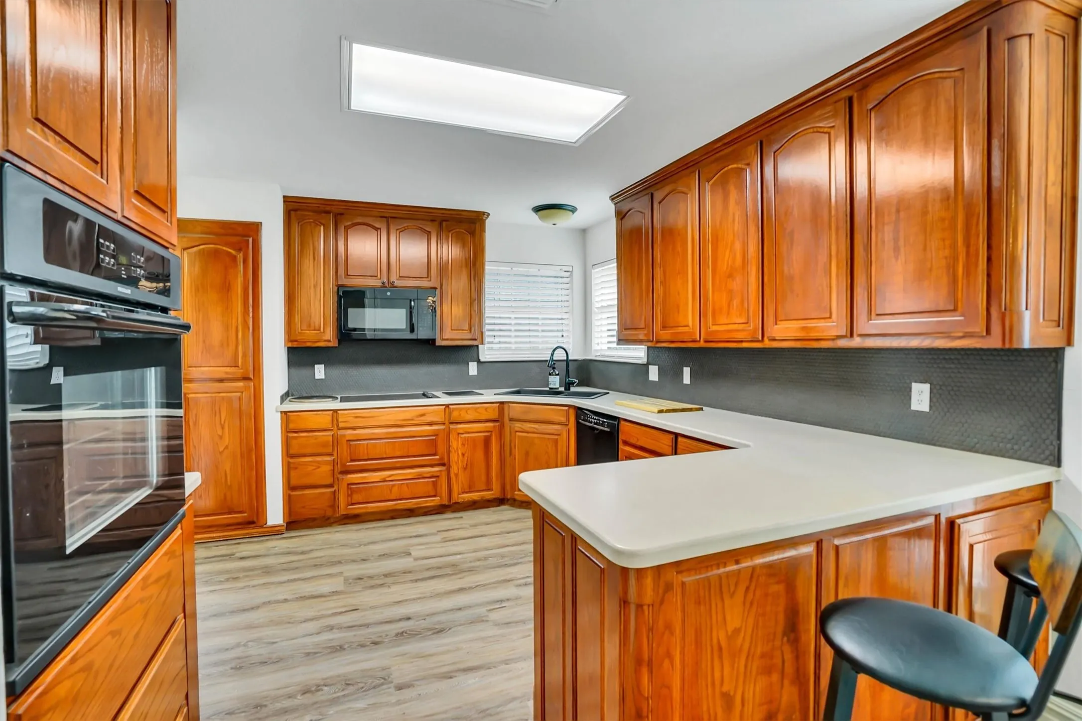 Kitchen featuring extensive wood cabinetry, light-toned countertops, a black tile backsplash, and wood-finish flooring