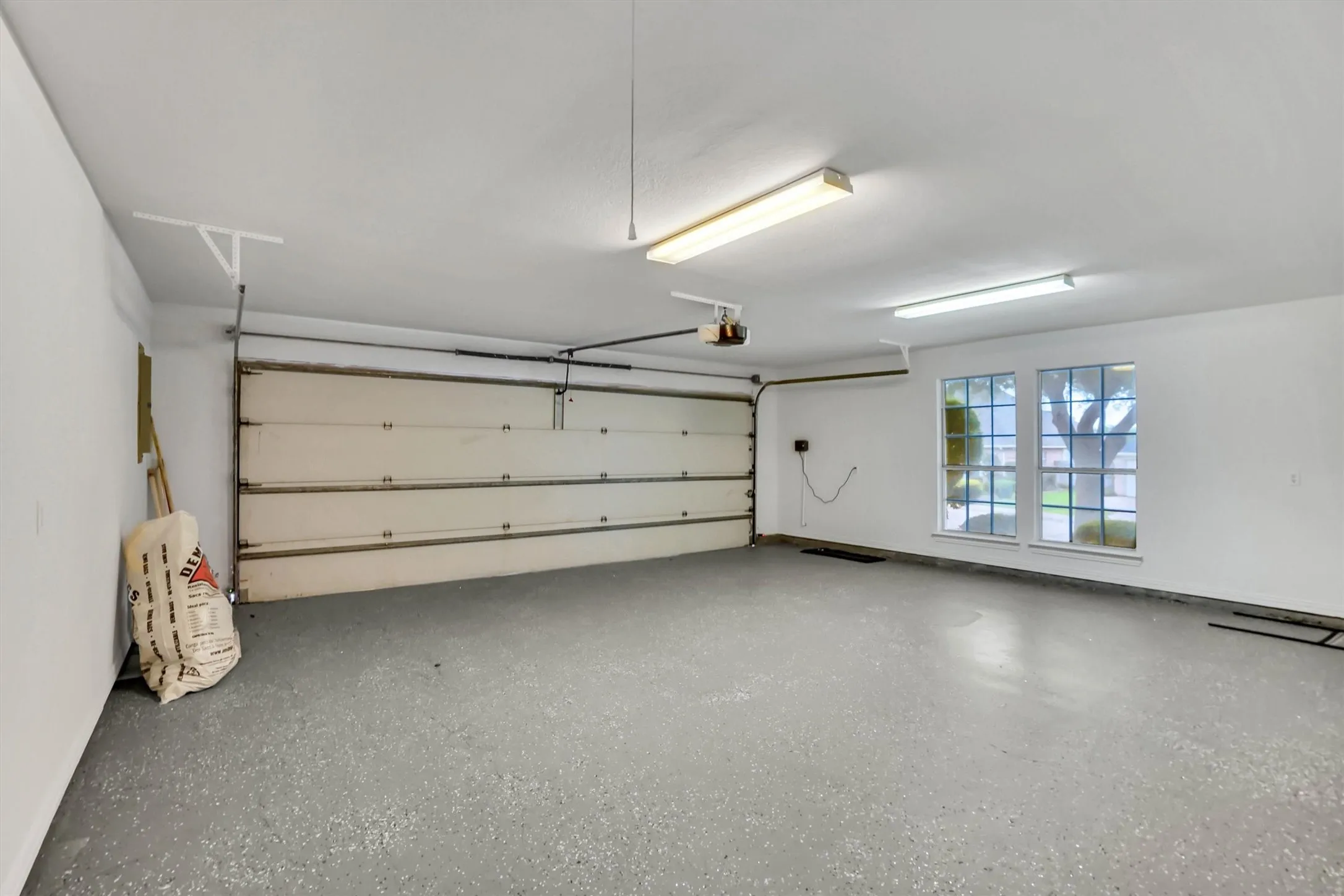 Spacious garage featuring a durable speckled epoxy floor, white painted walls, and ample overhead fluorescent lighting
