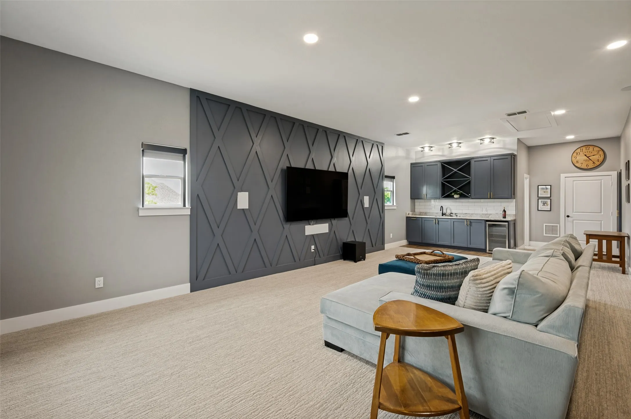 A striking custom accent wall creates a sophisticated focal point, while recessed lighting and large windows provide a bright and inviting atmosphere. The generous dimensions allow plenty of room for oversized furnishings and multiple seating areas, making it ideal for movie nights, game days, or gathering with friends and family. Wet bar with ample storage for friend gatherings and family movie nights. The door straight ahead leads to the attic.  The open doorway just past the wet bar is the upstairs full bath.