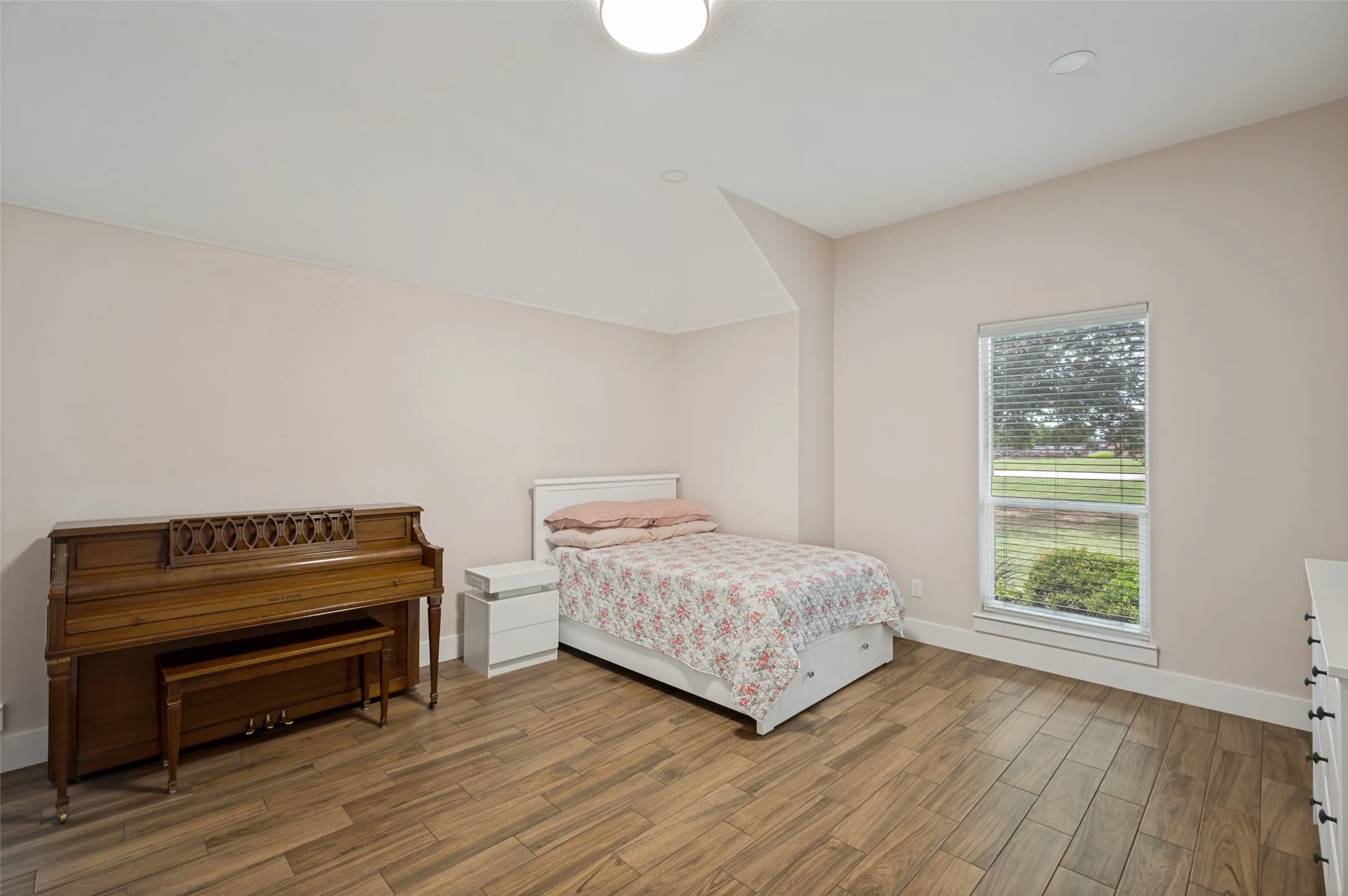 This spacious secondary bedroom offers a bright and versatile retreat with plenty of room to accommodate a variety of needs. The lovely wood-look tile continues into this room making for easy floor care without compromising beauty. Large windows invite natural light into the space while providing peaceful views of the surrounding property. The room features warm wood-look flooring, neutral designer finishes, and elevated ceilings that create an open and airy atmosphere. Generous proportions allow ample space for bedroom furnishings.