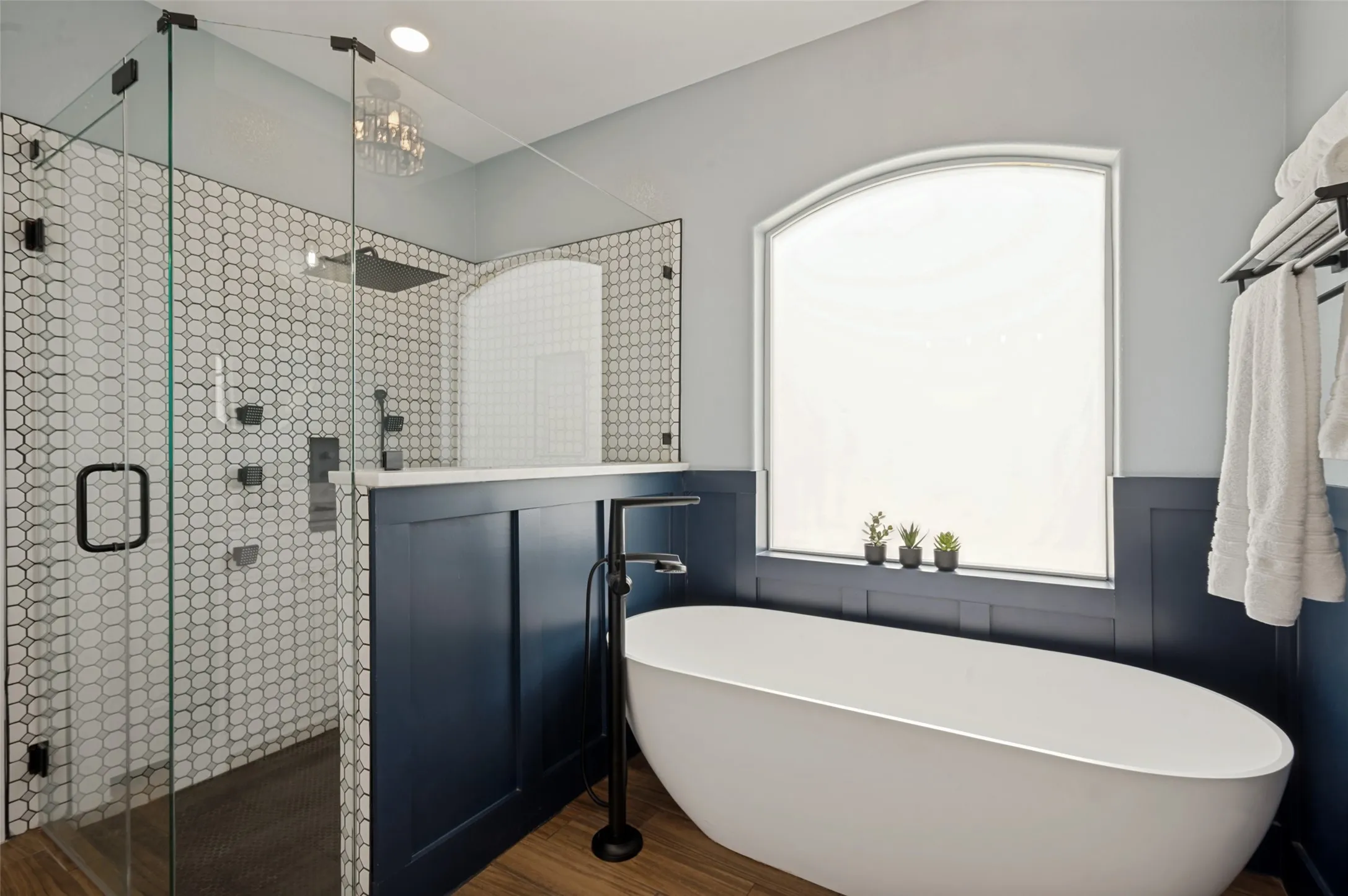 The expansive walk-in shower features floor-to-ceiling glass, stylish hexagon tile, and sleek matte black fixtures; the elegant stand alone soaking tub with floor-mounted hardware create a primary bath that is more than just a room--it's an experience. Natural light pours into the space, highlighting the thoughtful finishes and creating a bright, tranquil atmosphere. From the designer details to the spacious layout, every element of this primary bath has been carefully curated to provide comfort, luxury, and everyday indulgence.