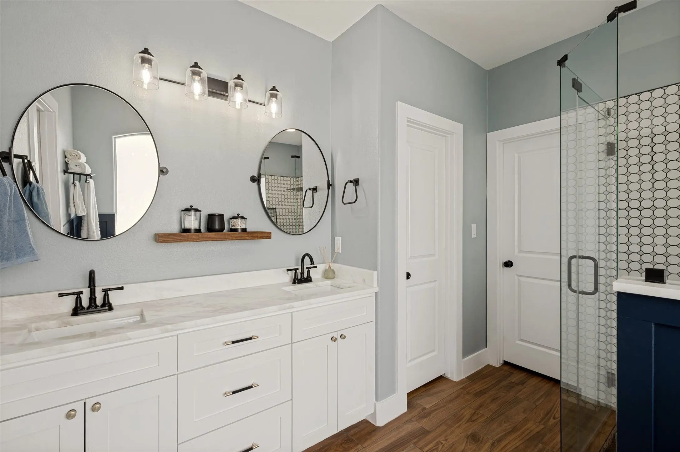 The spa-inspired primary bathroom combines modern elegance with thoughtful design, creating a luxurious retreat within the home. A spacious dual-sink vanity features crisp white cabinetry, sleek marble countertops, and stylish black fixtures that provide a striking contrast against the soft, neutral palette. Oversized round mirrors and contemporary vanity lighting add a designer touch while enhancing the bright, airy feel of the space. Adjustable mirrors, private toilet, and large walk-in closet make the space so easy to use.