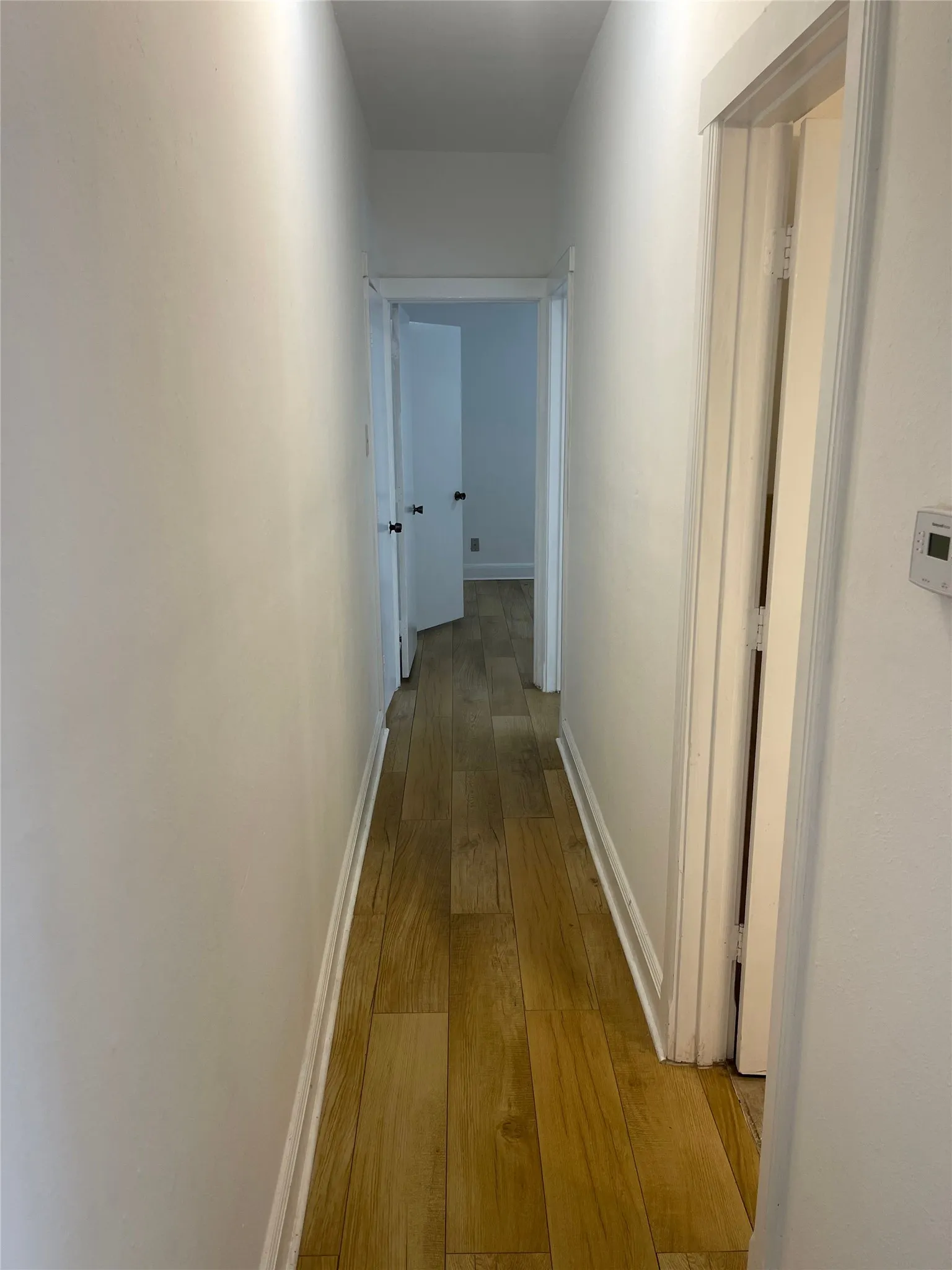 Hallway featuring wood-finish flooring, white baseboards, and neutral wall paint