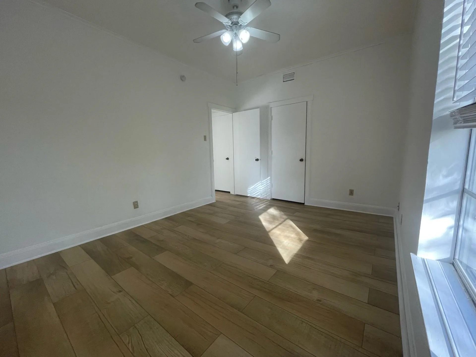 Spacious room featuring light wood-finish flooring, white walls, and a ceiling fan with integrated lighting