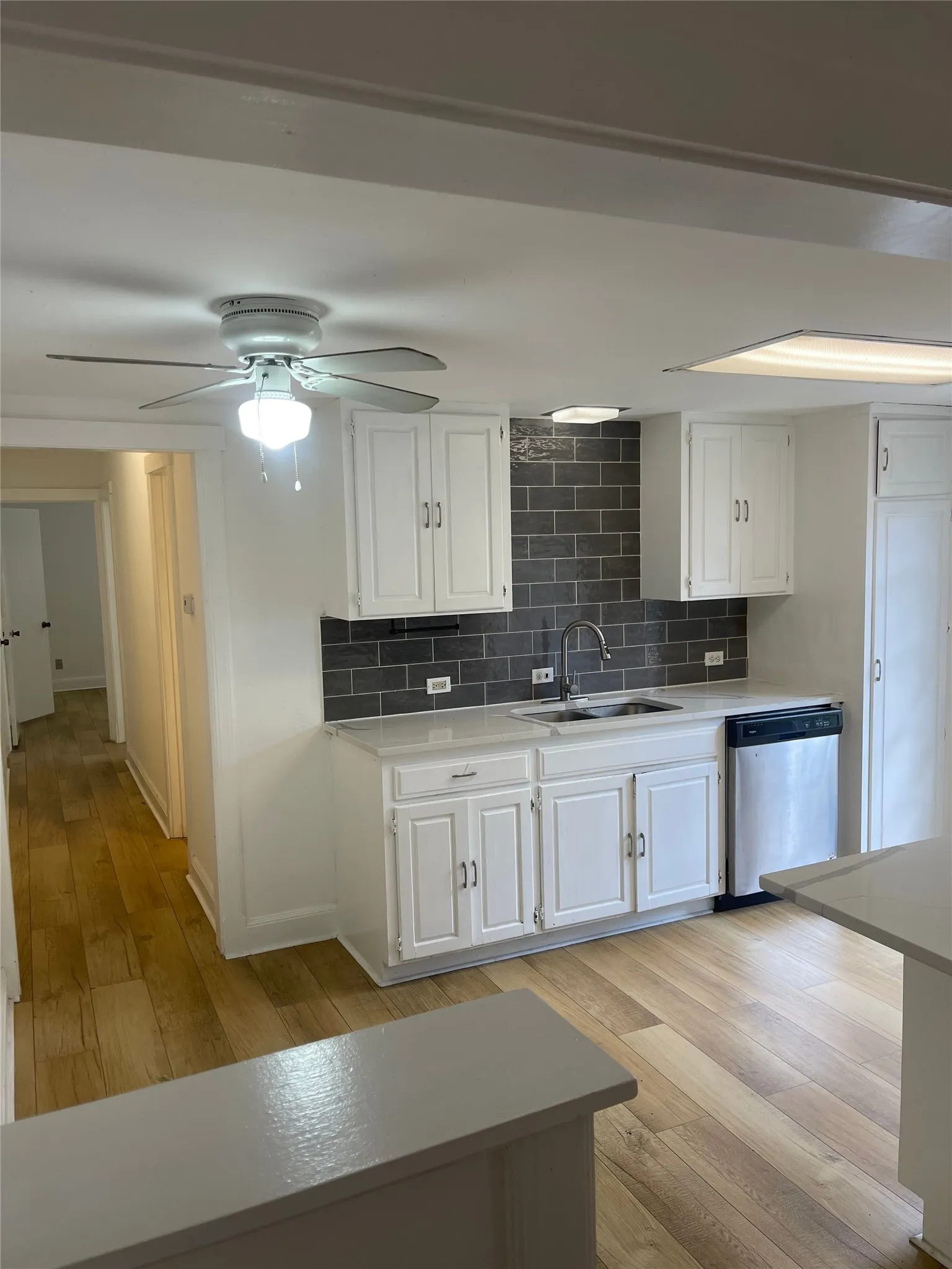 Kitchen featuring white cabinetry, grey subway tile backsplash, stainless steel sink, and a built-in dishwasher