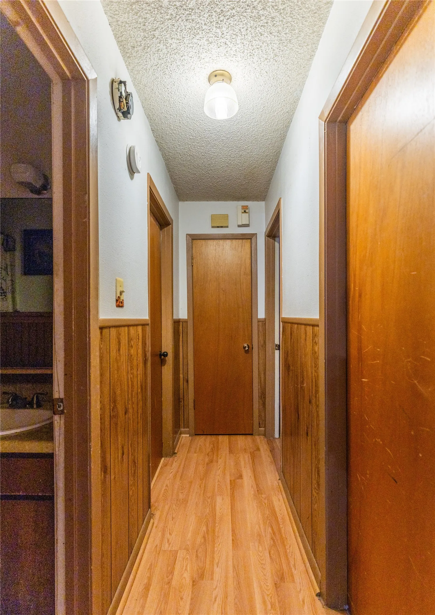 Hallway featuring wood-finish flooring, wood paneling, and a flush-mount ceiling light fixture