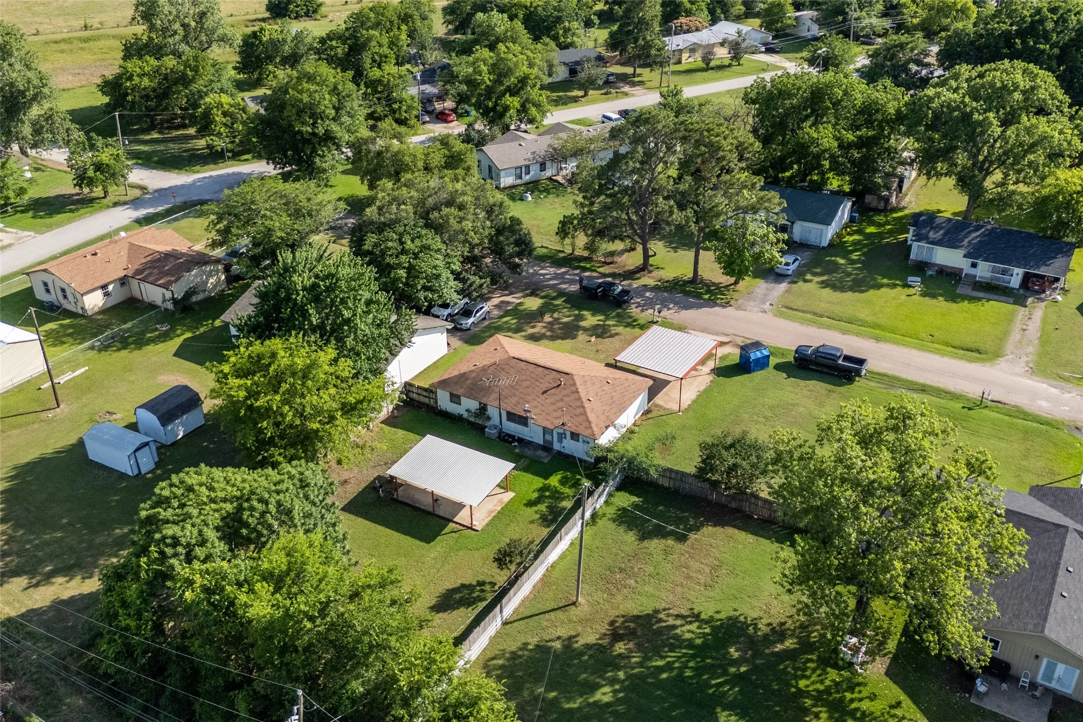 Single-story residence featuring a brown shingle roof, two detached carports with metal roofs, and a fenced perimeter