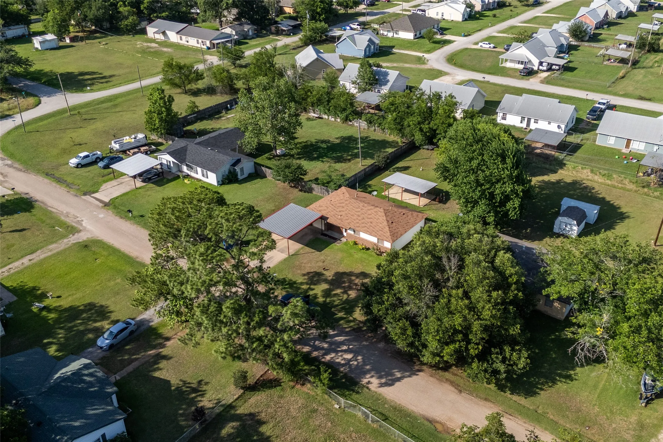 Aerial perspective highlighting a residential property with a brown shingle roof and a covered carport