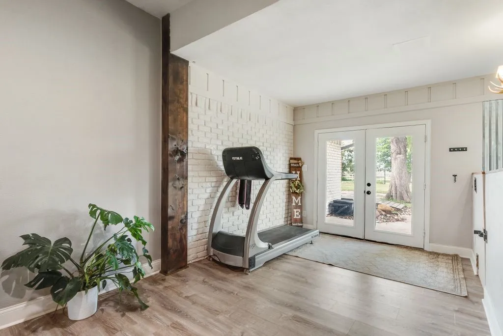 Spacious room featuring light wood-finish flooring and a white painted brick accent wall