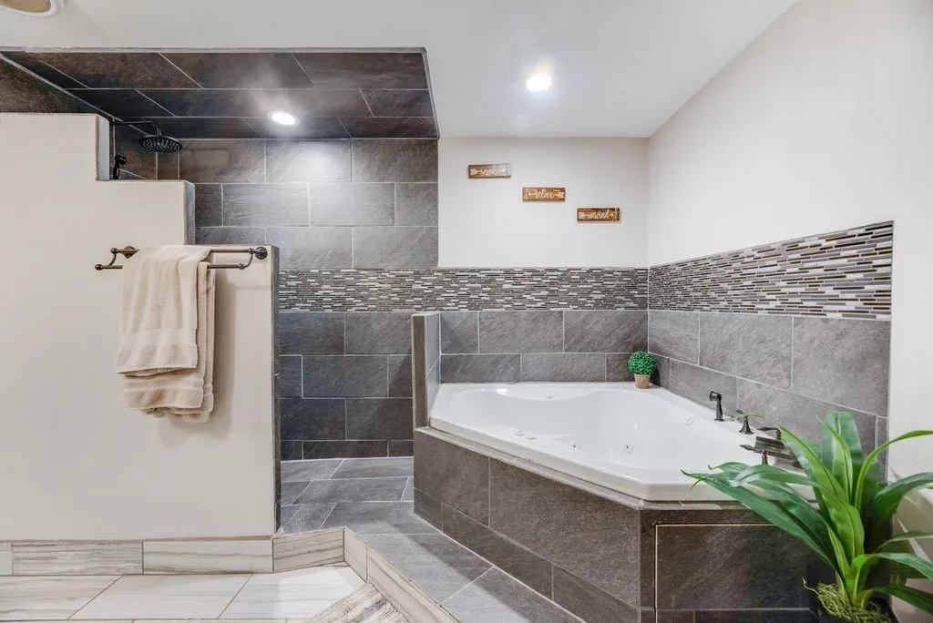 Bathroom featuring a jetted corner tub with dark tile surround, a walk-in shower with a rain showerhead, and a mosaic tile accent band