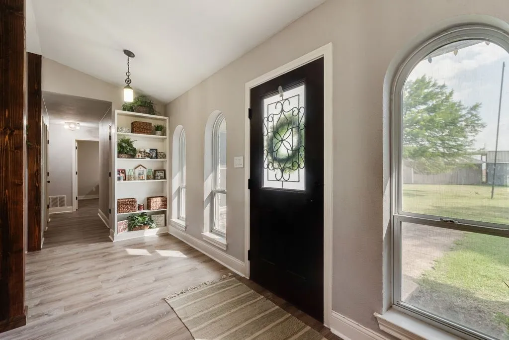 Entryway featuring a dark wood-finish door with decorative glass, wood-finish flooring, built-in shelving, and multiple arched windows