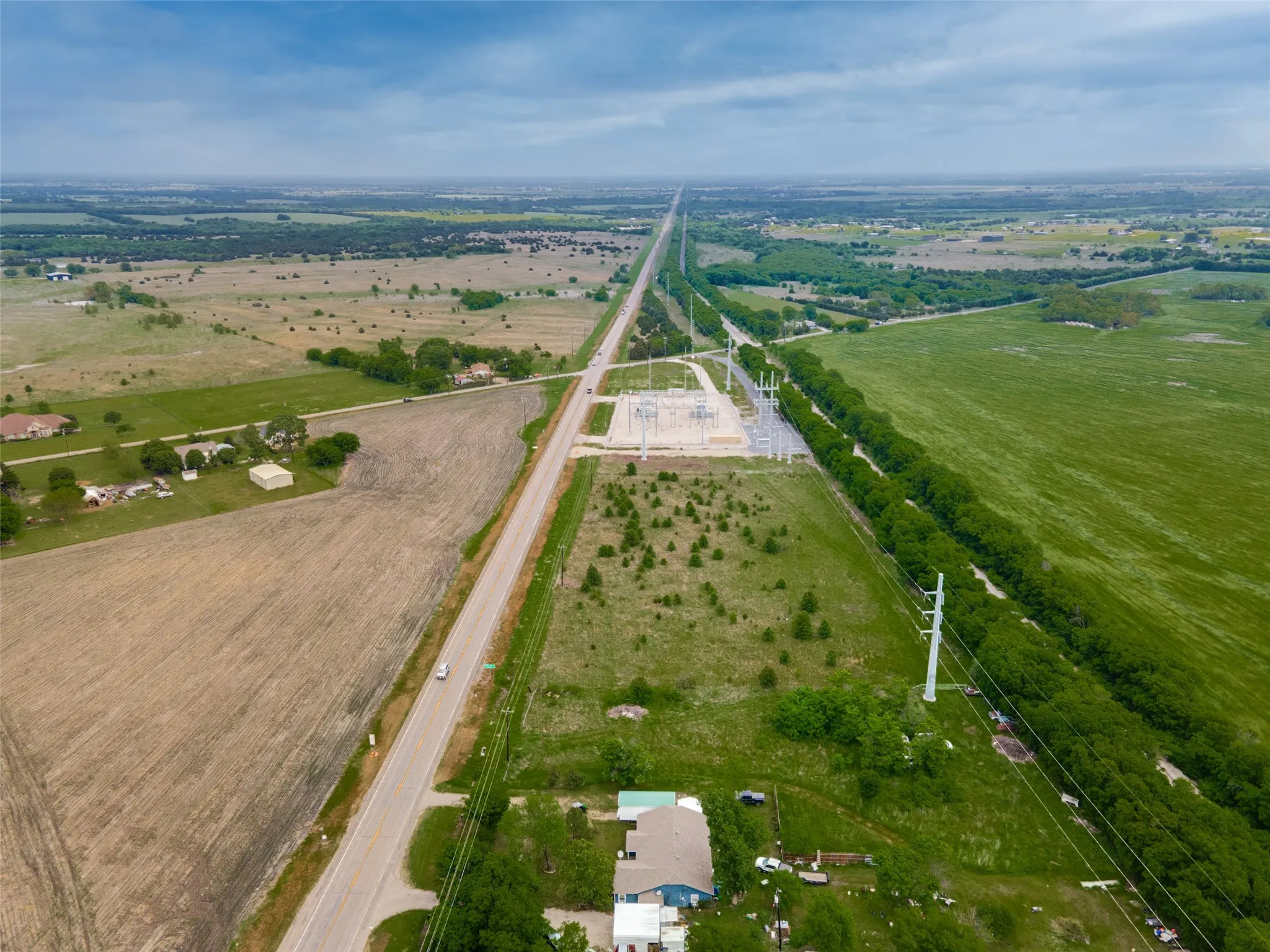 Expansive aerial perspective showcasing a rural landscape with a long road bisecting diverse terrain