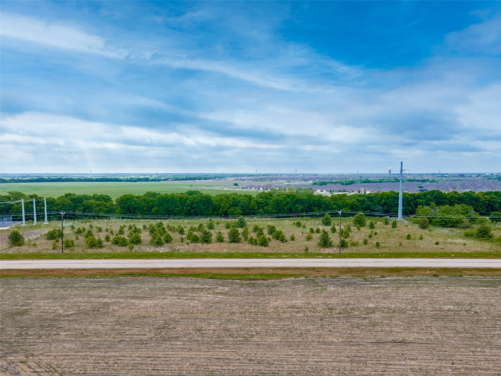 Expansive undeveloped land featuring a cleared foreground, a paved road, and a distant tree line