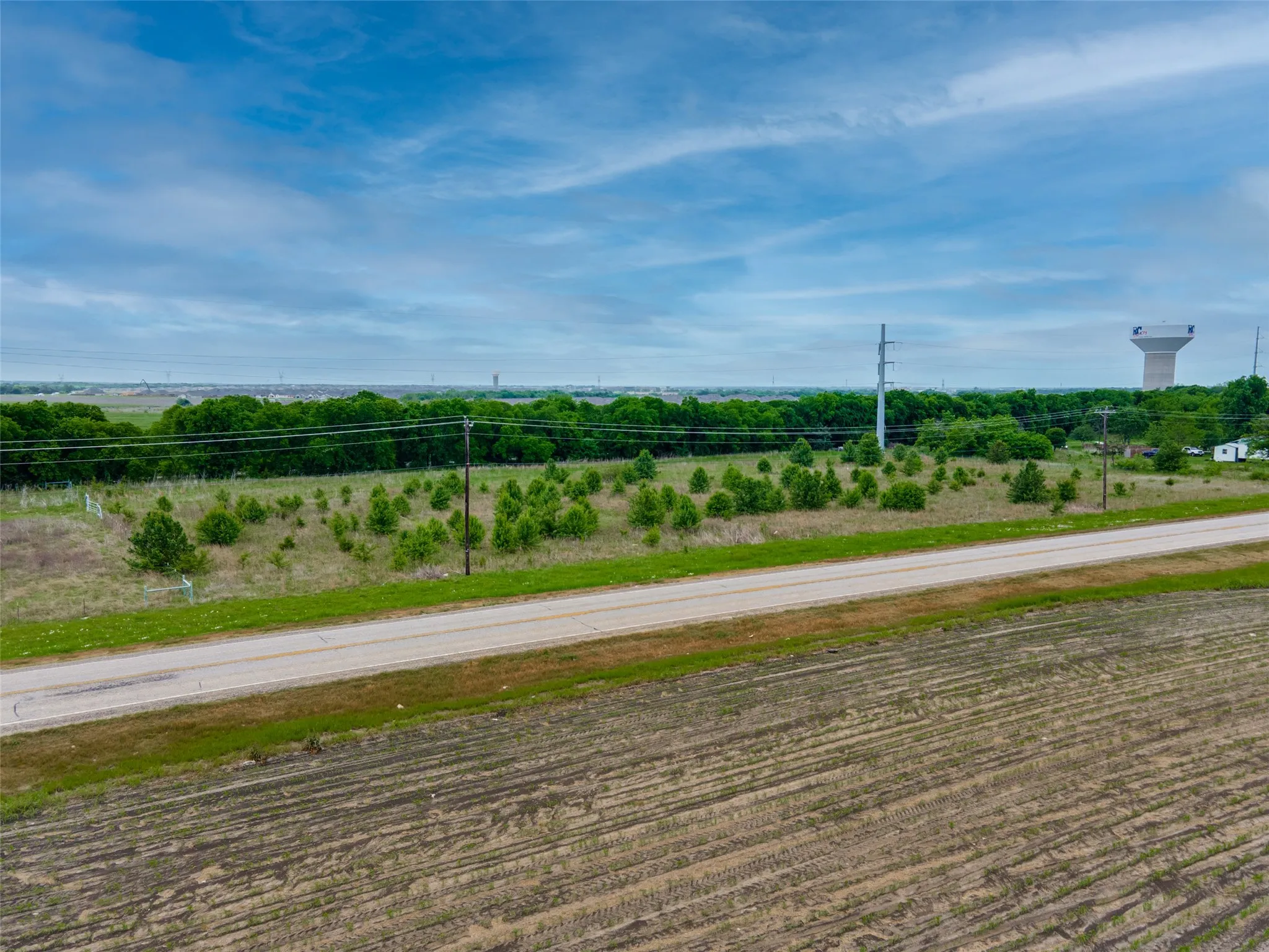 Expansive open land featuring diverse vegetation, a paved road, and utility infrastructure
