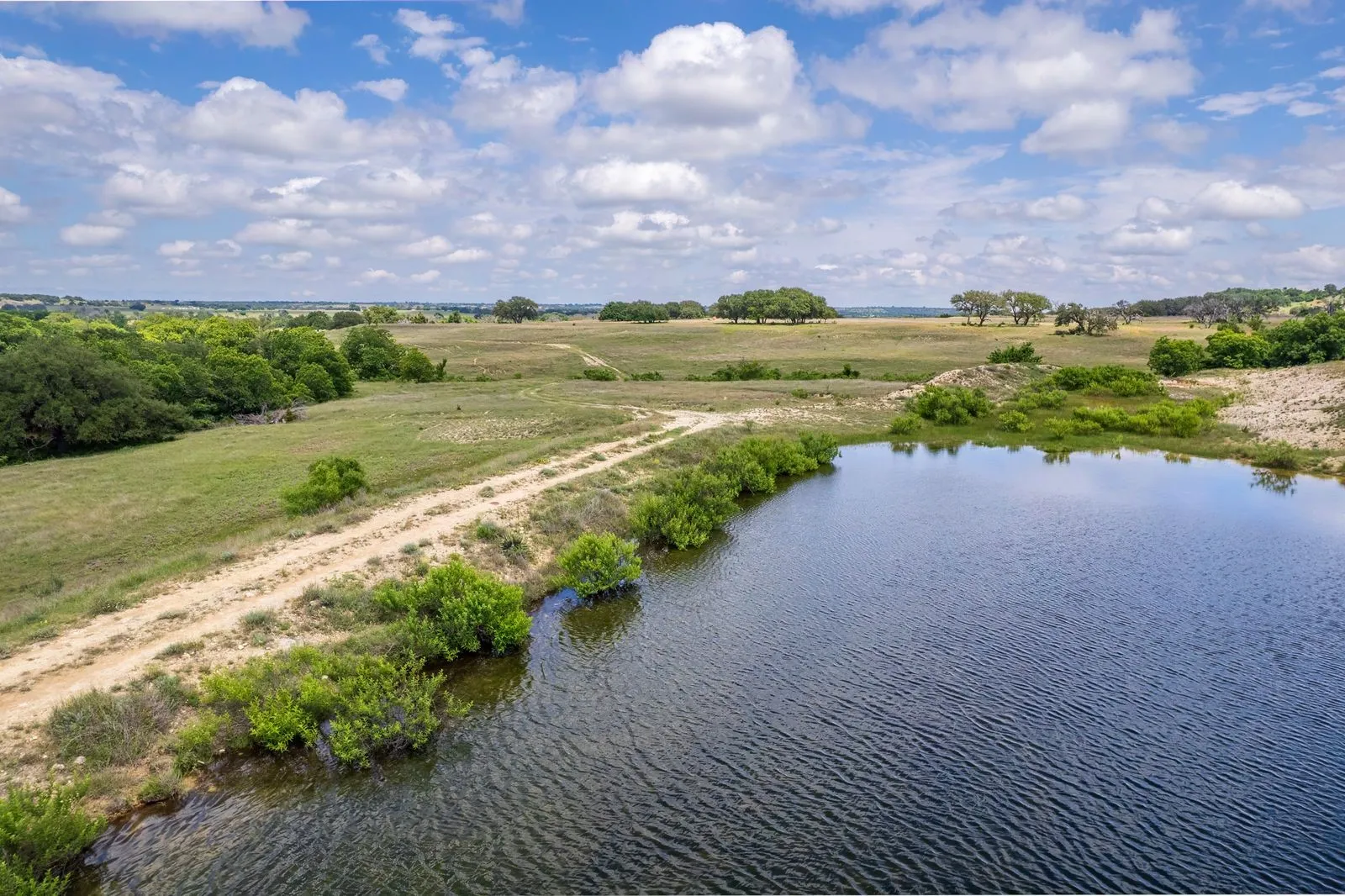 Expansive open land with a large pond, natural terrain, and distant tree lines