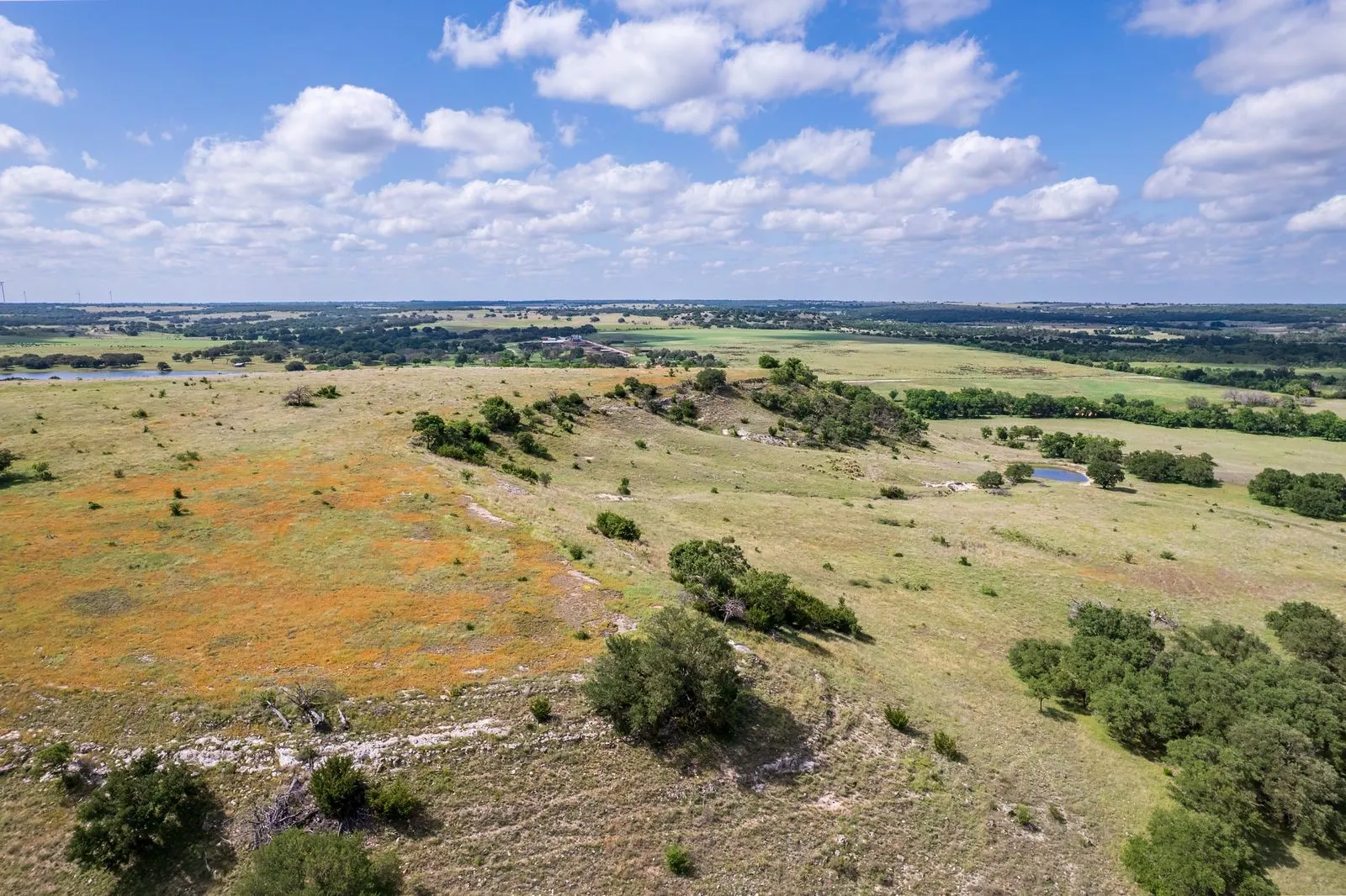 Expansive acreage featuring a diverse landscape of rolling hills, scattered trees, and a pond