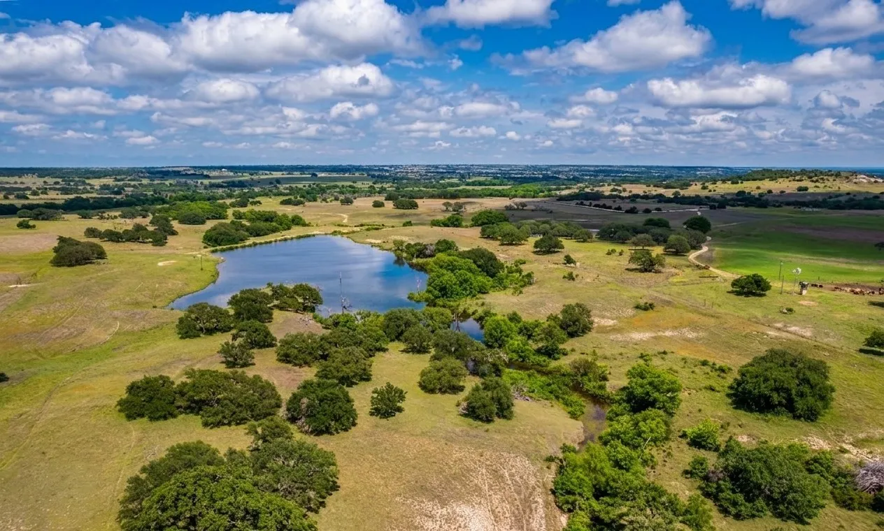 Expansive acreage featuring a central pond, rolling topography, scattered mature trees, and open pastures
