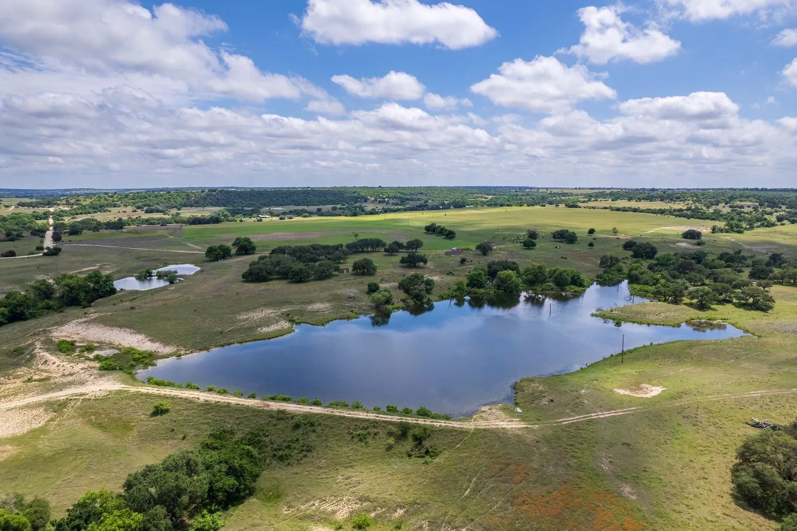 Expansive land featuring a large pond surrounded by green fields and scattered trees