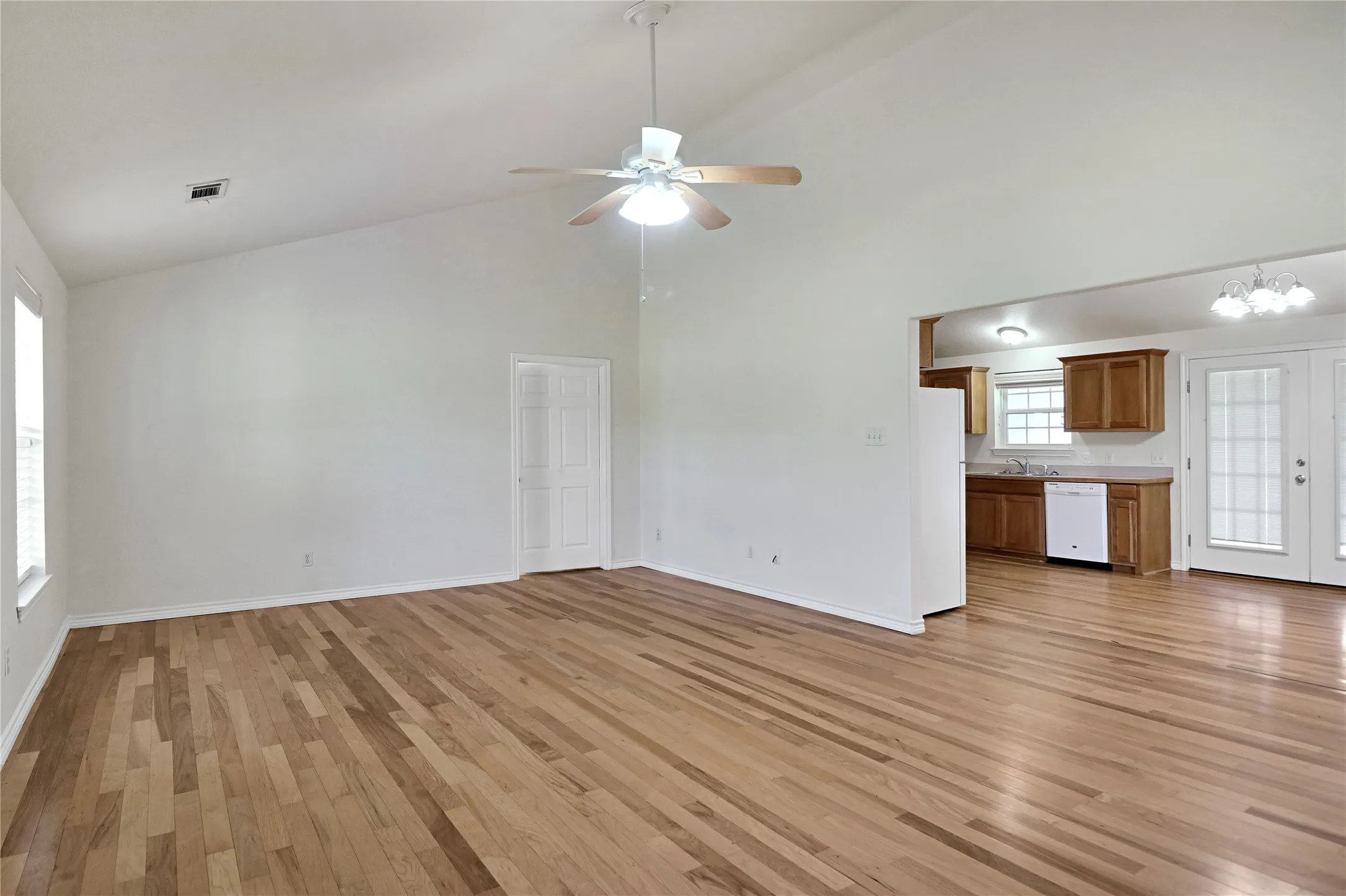 Open-concept living area featuring wood-finish flooring, a vaulted ceiling, and a ceiling fan with integrated lighting