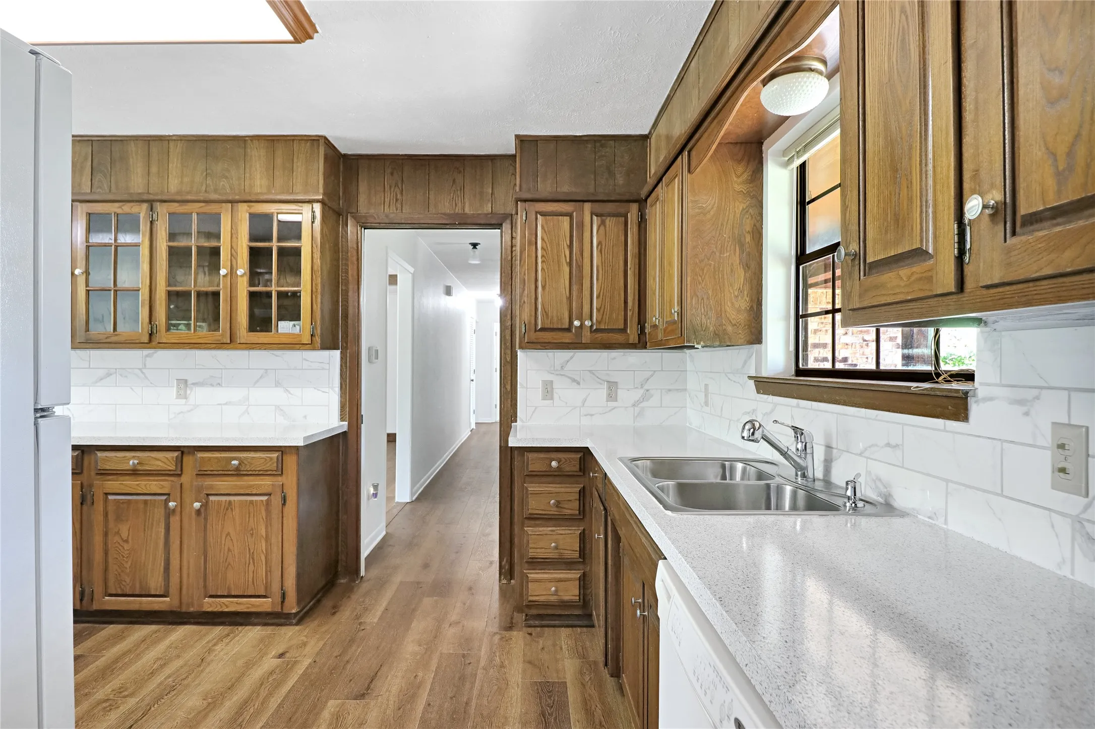 Kitchen featuring wood-finish cabinetry, white subway tile backsplash, light-colored countertops, and wood-finish flooring