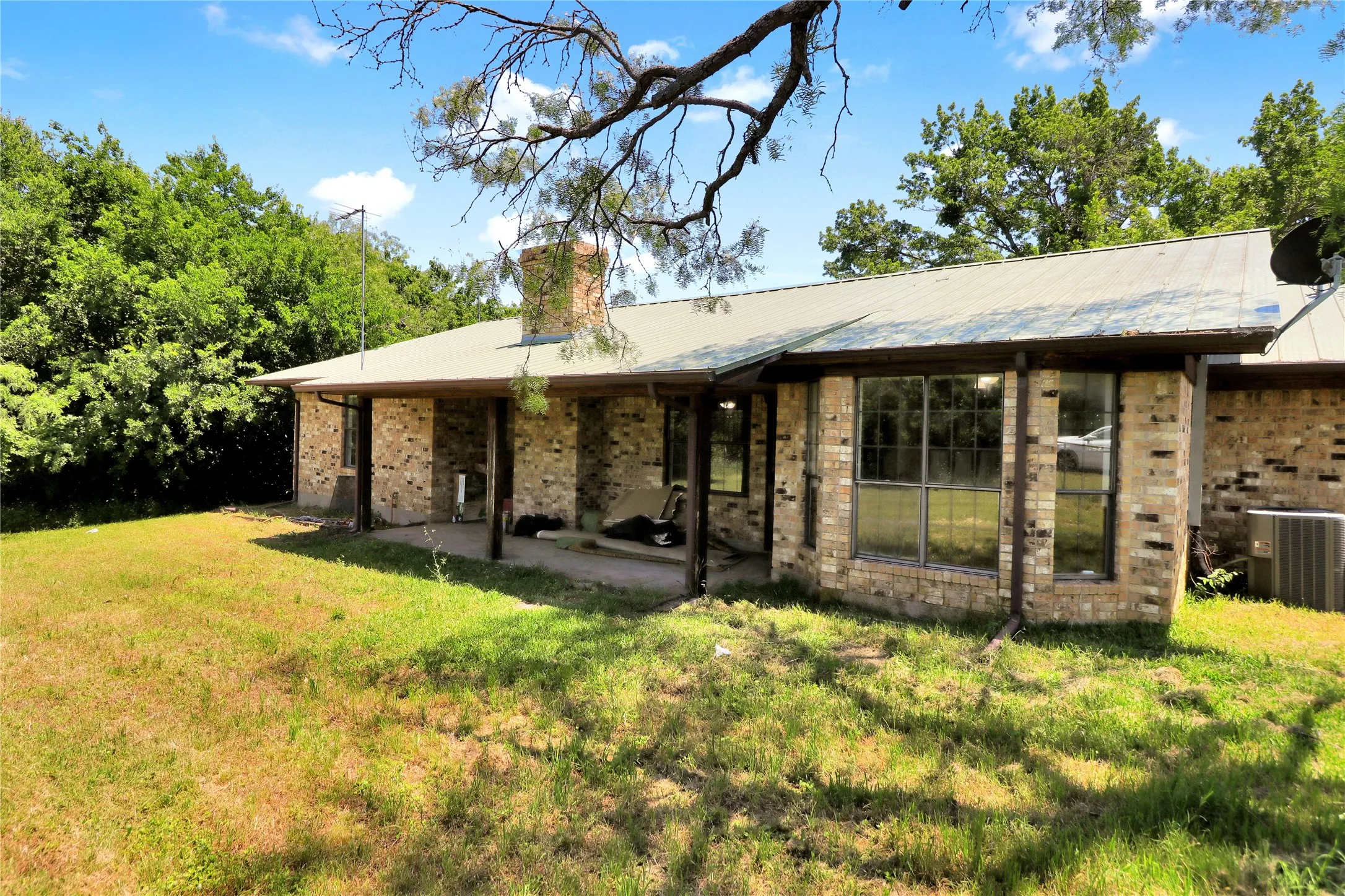 Brick exterior featuring a metal roof, covered patio, and mature trees