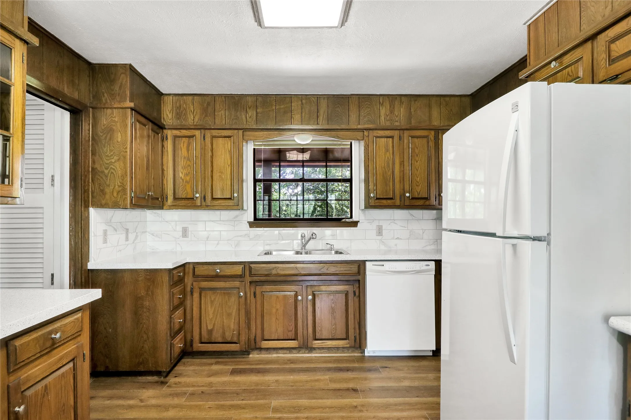 Kitchen featuring wood-finish cabinetry, solid surface countertops, white subway tile backsplash, and wood-finish flooring
