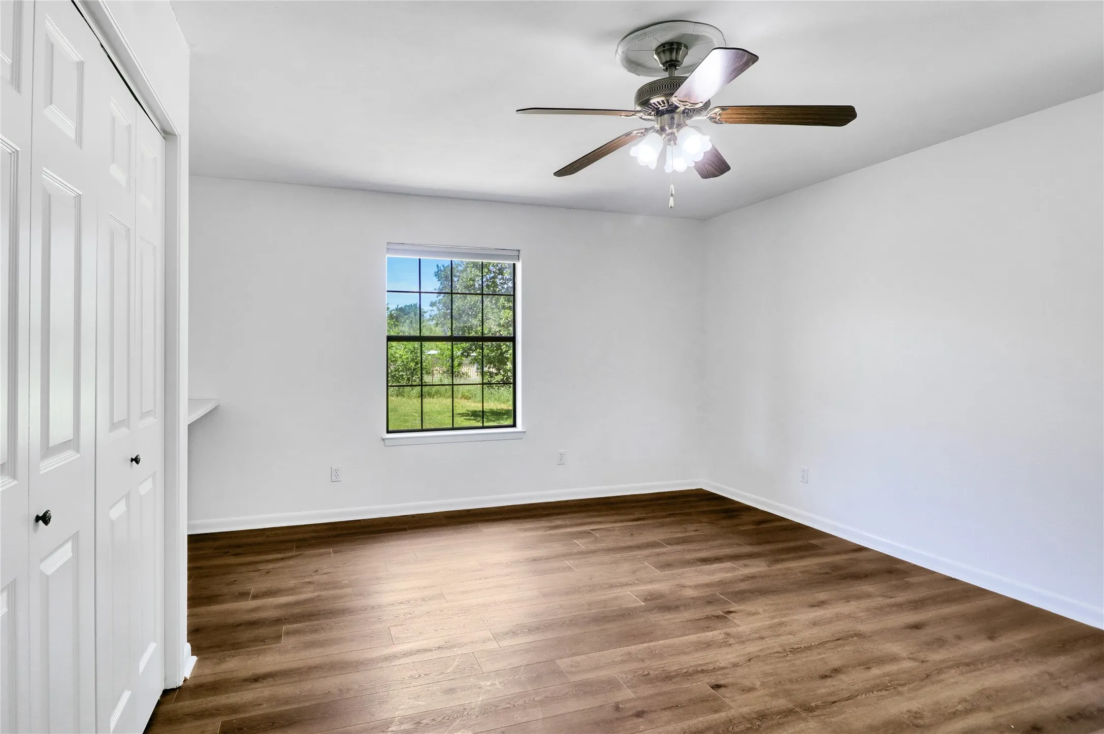 Wood-finish flooring, white walls, ceiling fan, and a window providing natural illumination