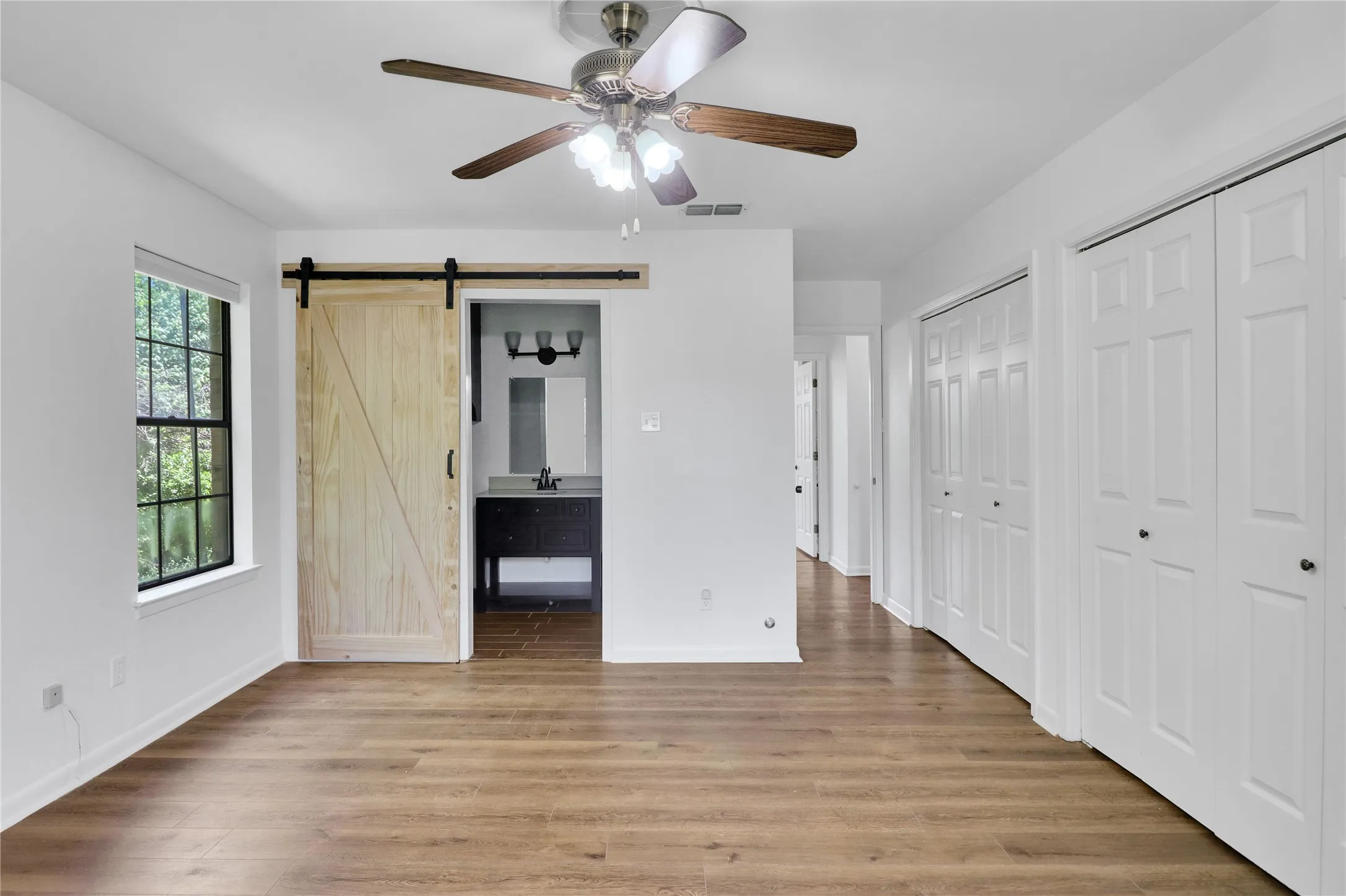 Spacious room featuring wood-finish flooring, a ceiling fan with integrated lighting, and multiple white bi-fold closet doors