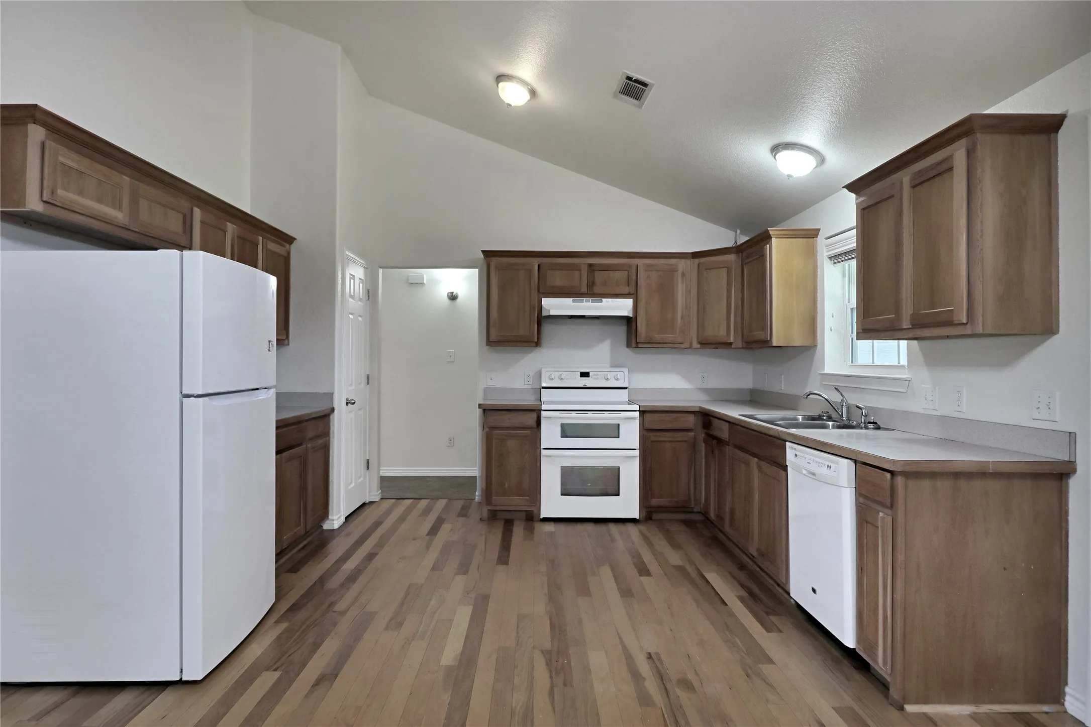 Kitchen featuring wood-finish cabinetry, white appliances, light countertops, and wood-finish flooring