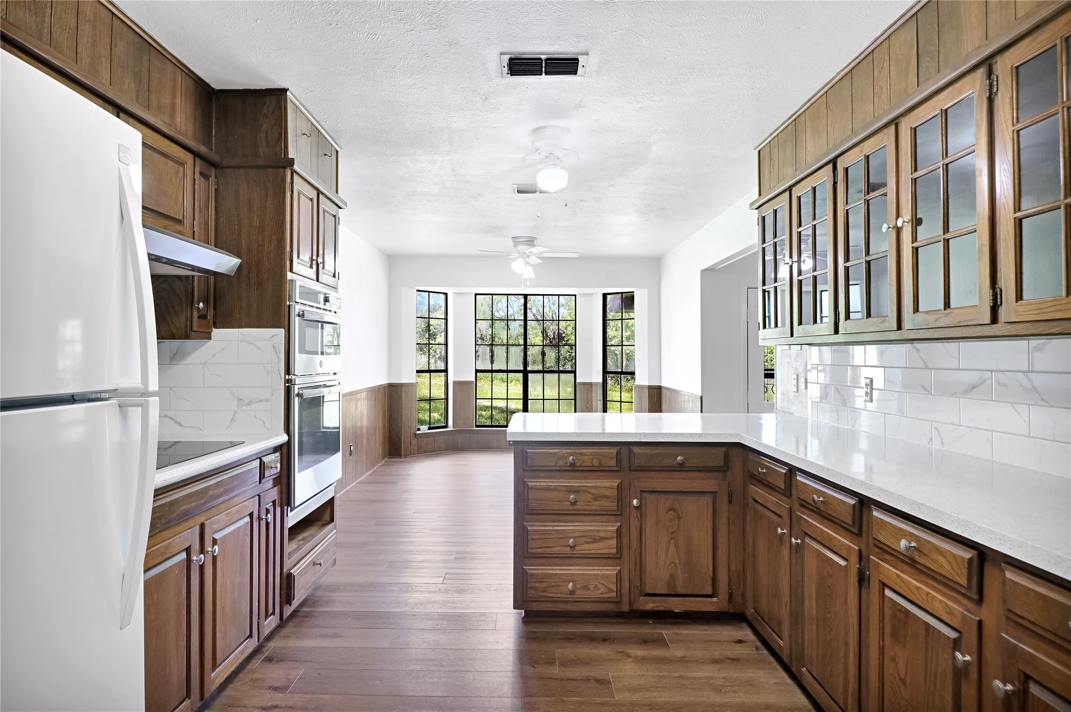 Kitchen featuring wood-finish cabinetry, quartz countertops, white subway tile backsplash, and wood-finish flooring