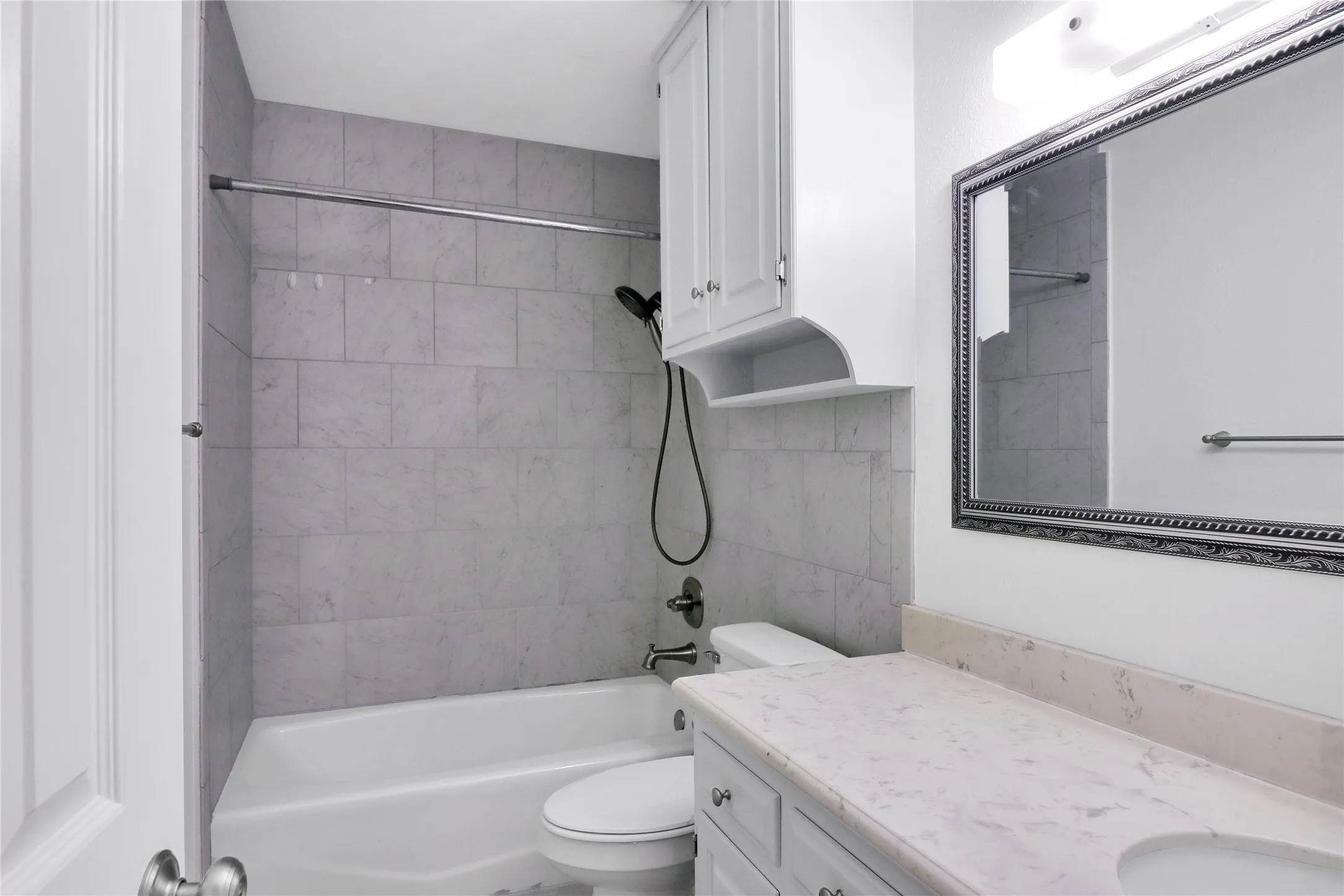 Bathtub and shower combination with tiled surround, vanity with light-toned countertop, integrated sink, and white cabinetry