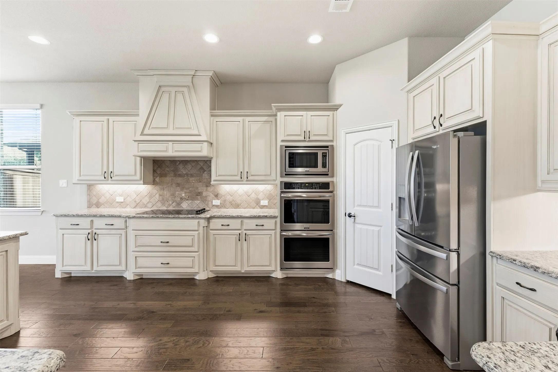 Chef's kitchen featuring custom cream cabinetry with detailed trim, stainless steel dual wall ovens and microwave, a coordinating hood range, quartz countertops, subway tile backsplash, and a large center island