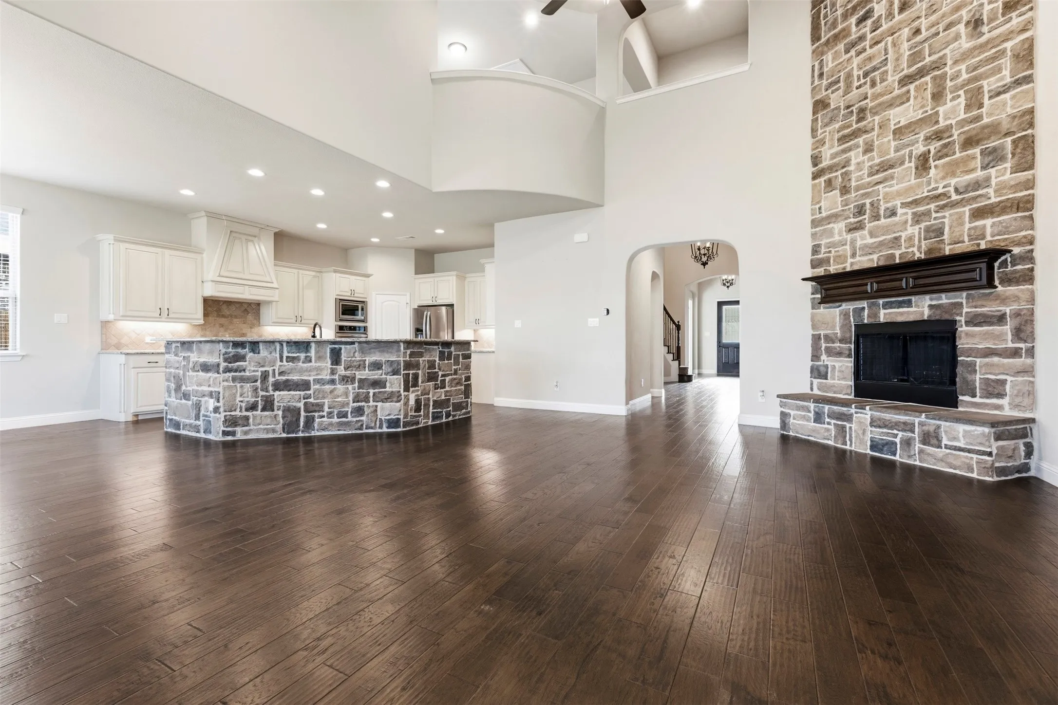 Open-concept living space featuring soaring vaulted ceilings with recessed lighting, dark wood-finish flooring throughout, and a two-sided fireplace with stacked stone surround