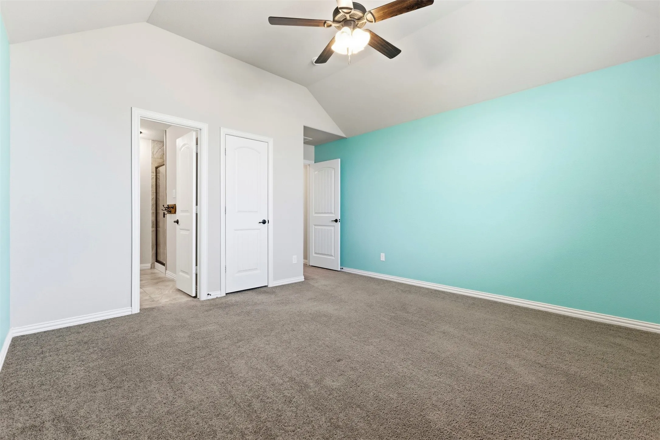 Vaulted ceiling with a ceiling fan, plush carpet flooring, and multiple interior doors