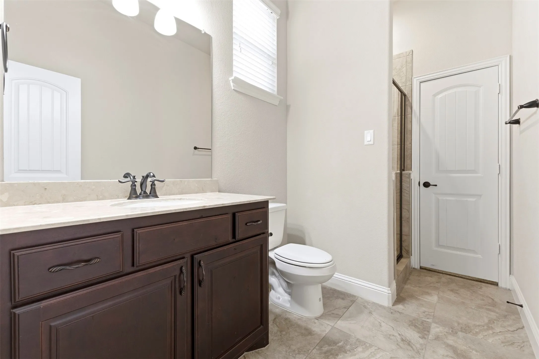 Spacious bathroom featuring a dark wood-finish vanity with dual sink configuration, brushed nickel hardware, and stone-finish flooring
