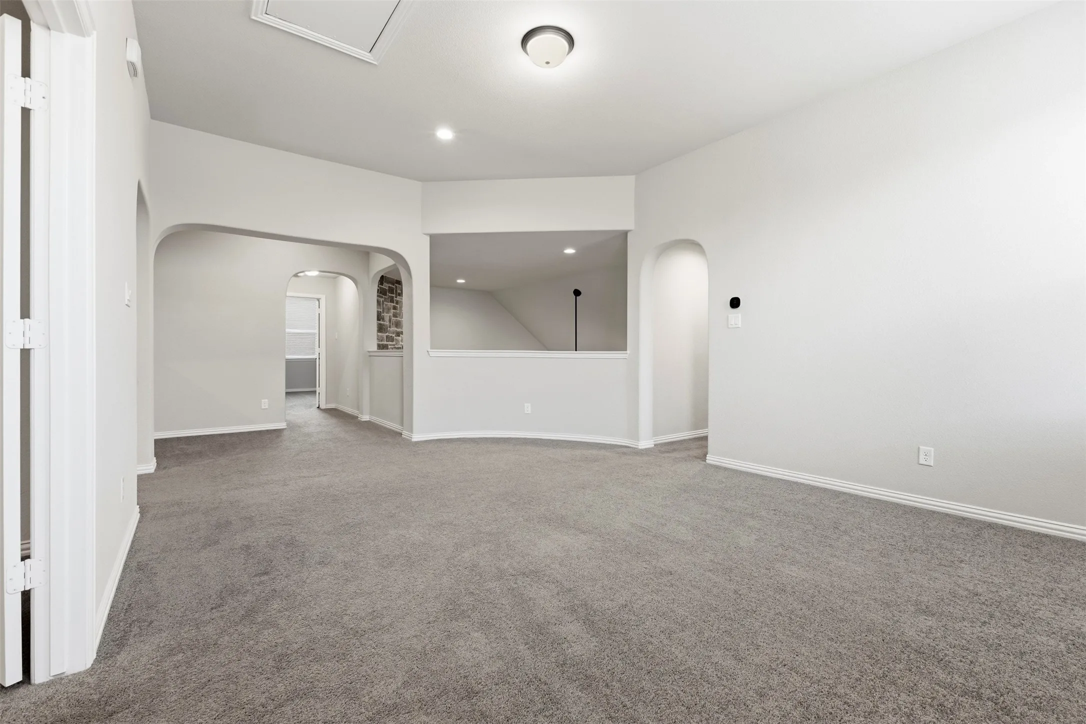 Expansive room featuring plush gray carpeting, arched doorways, a half-wall partition, and recessed lighting