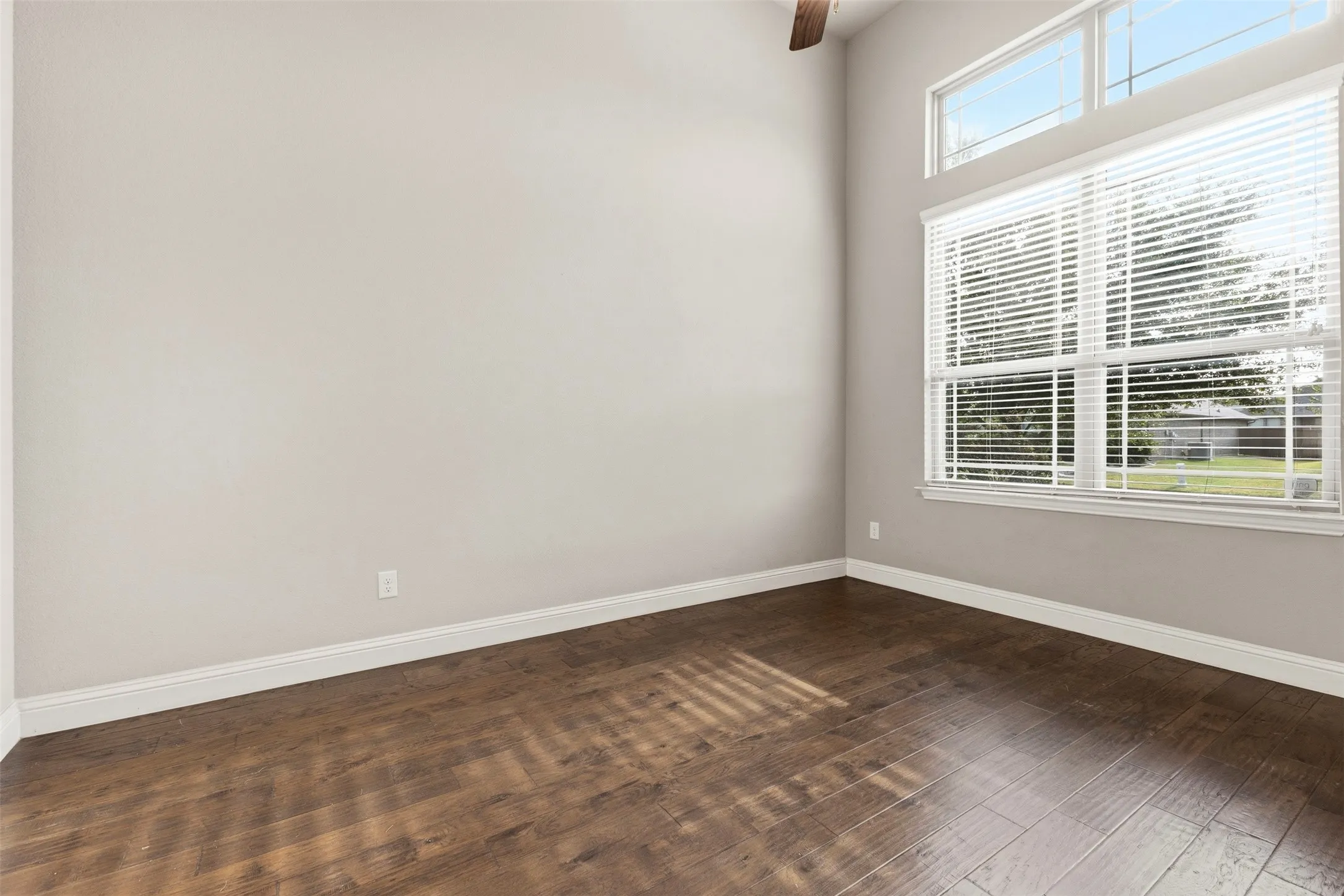 Bright, light-filled room featuring expansive windows with plantation shutters, abundant natural light, and warm wood-finish flooring throughout