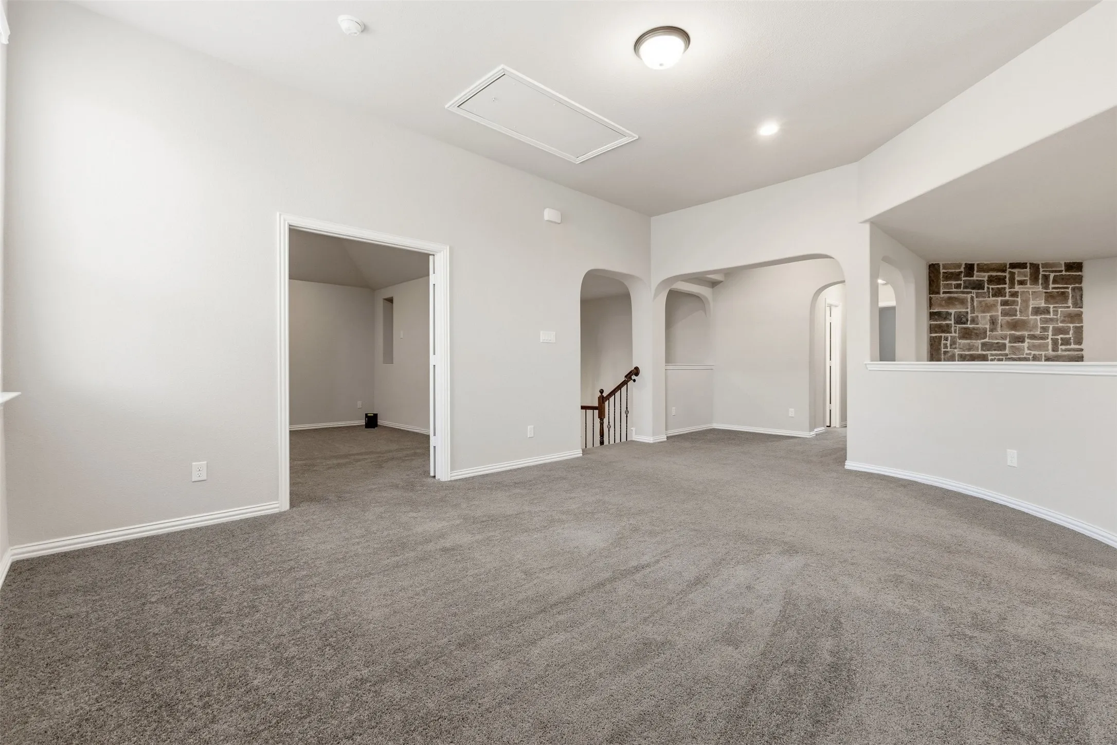 Spacious open-concept recreation room with neutral gray carpet flooring, recessed ceiling lighting, and multiple architectural apertures including arched doorways