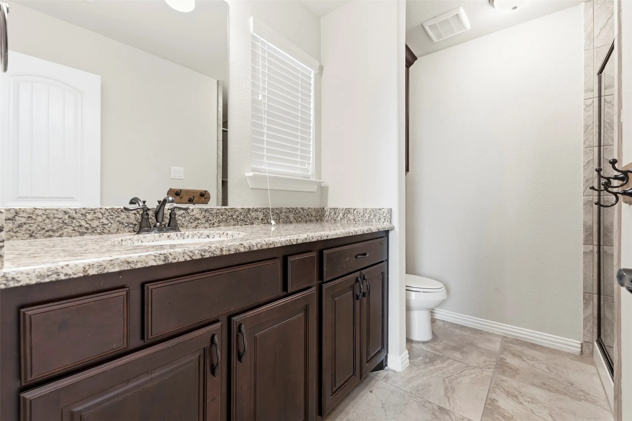 Spa-inspired master bathroom featuring rich espresso cabinetry with ample storage, granite countertops, dual vanity sinks with chrome fixtures, and a walk-in shower with tile surround and glass enclosure