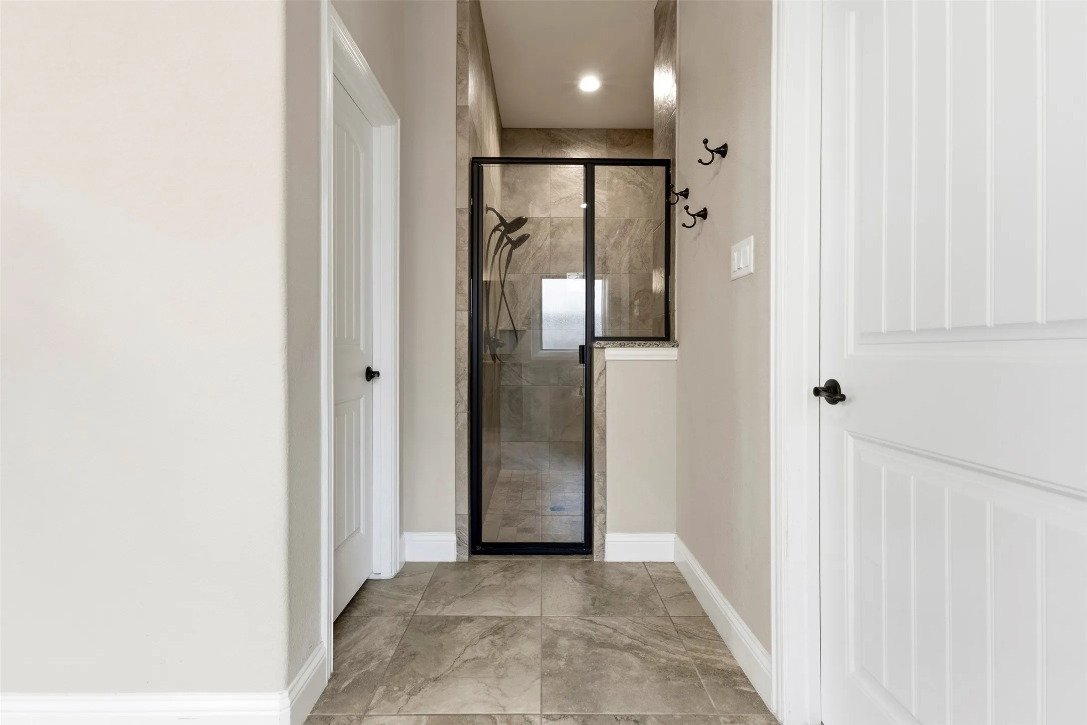 Tiled flooring leading to a glass-enclosed shower with a dark frame and tiled walls