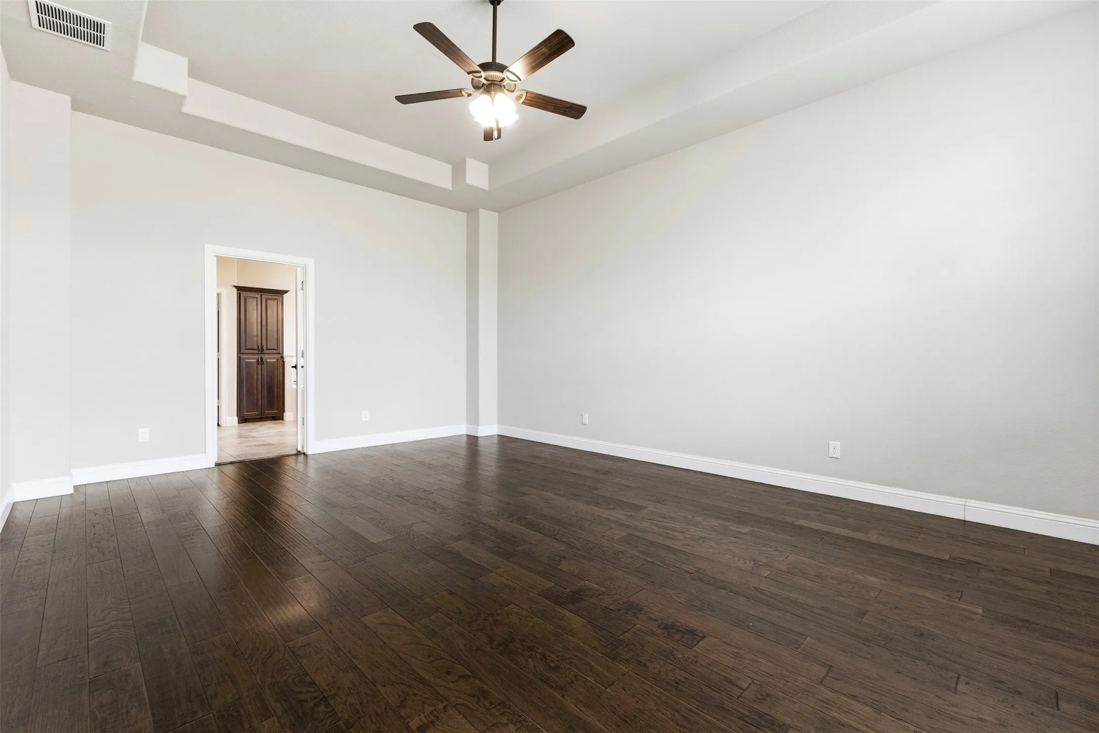 Spacious room featuring rich wood-finish flooring, white walls, and high ceilings with a ceiling fan and recessed lighting