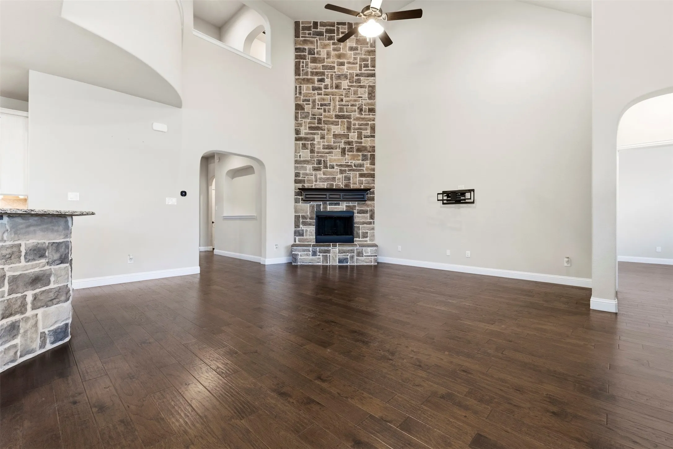 Soaring ceiling, stone-clad fireplace, wood-finish flooring, and arched doorways