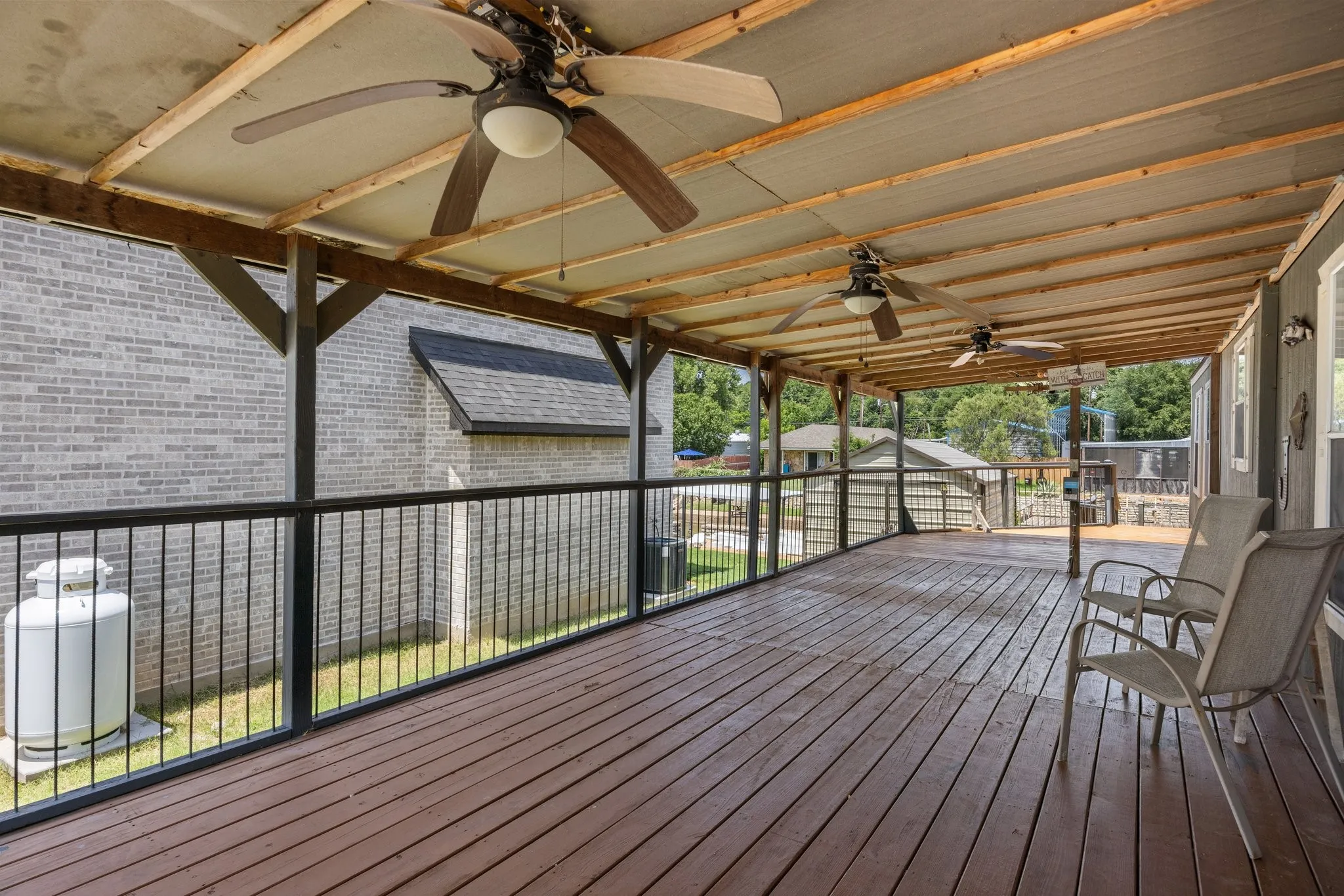 Covered deck featuring wood-finish flooring, multiple ceiling fans, exposed wood beams, and dark metal railings