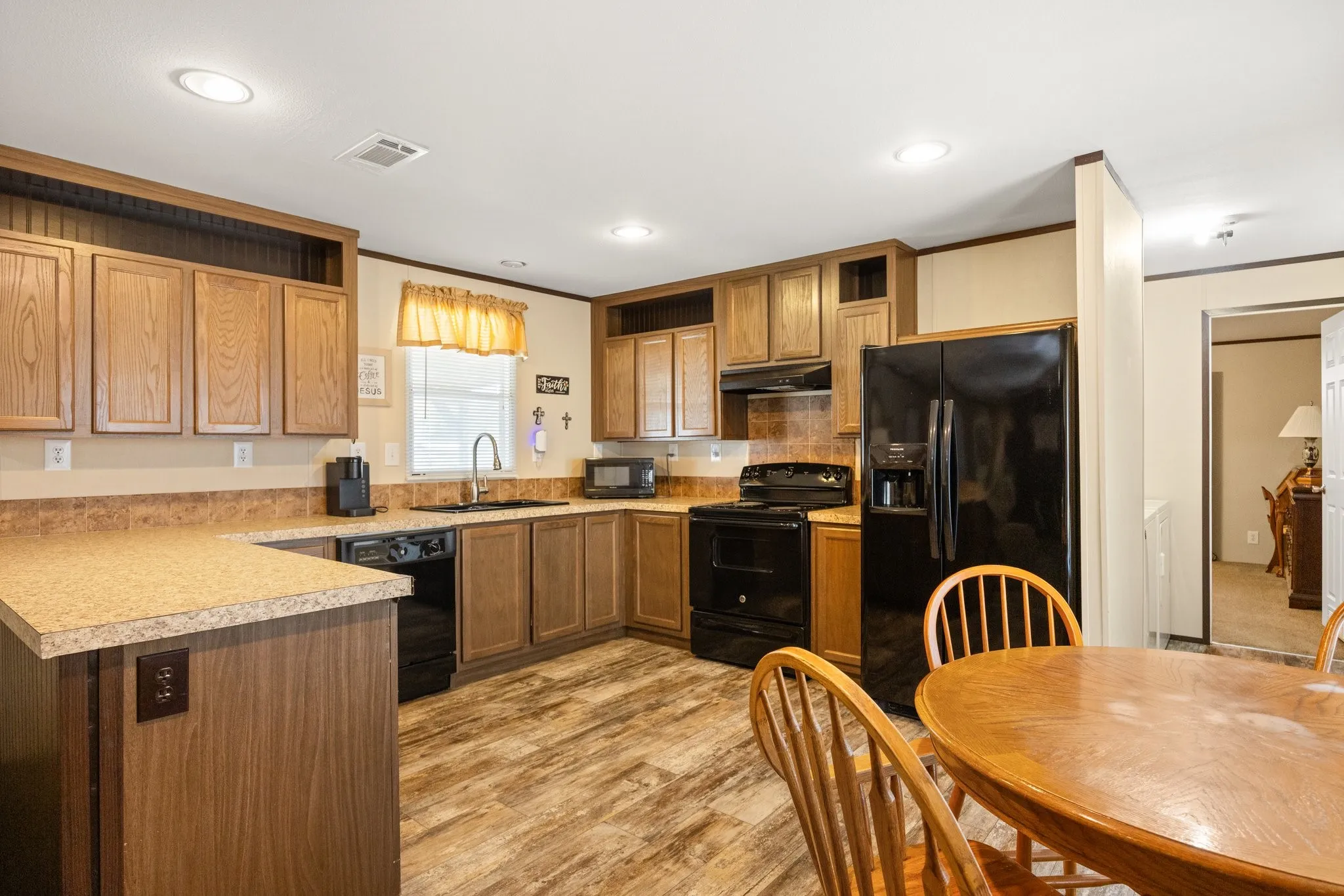 Well-appointed kitchen featuring wood-finish cabinetry, black appliances, a U-shaped countertop, recessed lighting, and wood-finish flooring