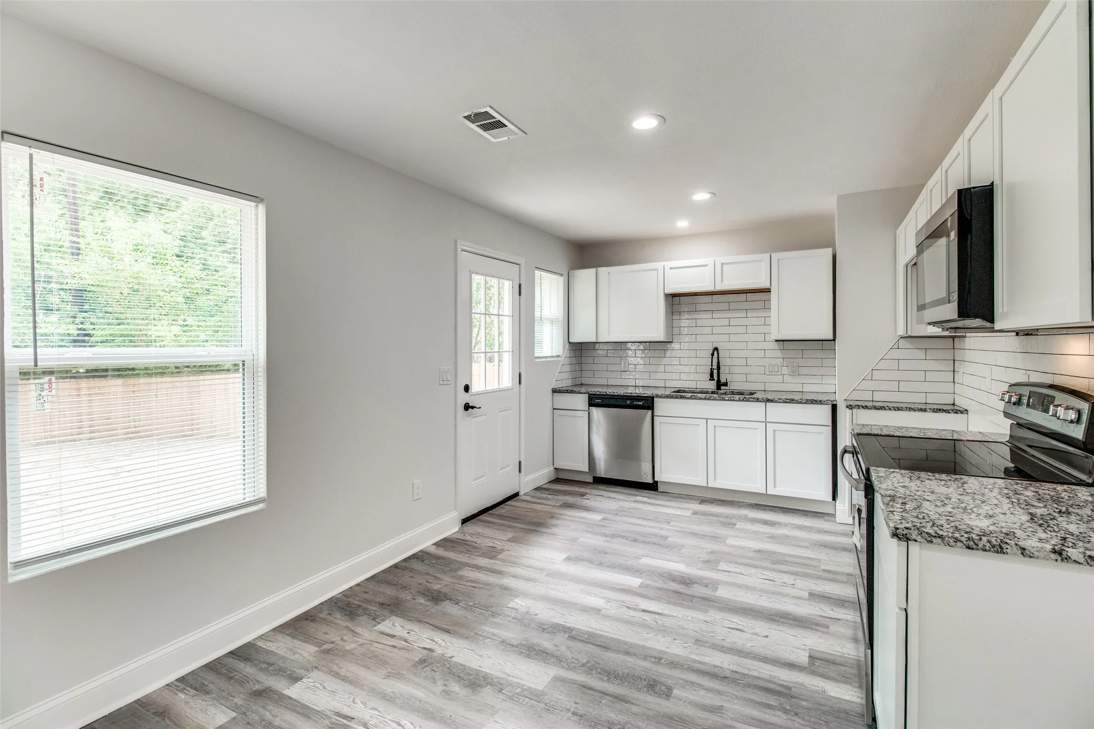 Kitchen with light stone counters, stainless steel appliances, sink, white cabinets, and light hardwood / wood-style flooring