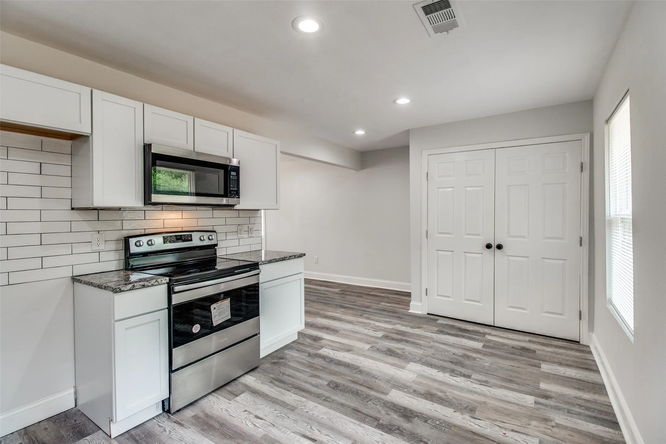 Kitchen with stainless steel appliances, dark stone countertops, white cabinets, and light hardwood / wood-style flooring