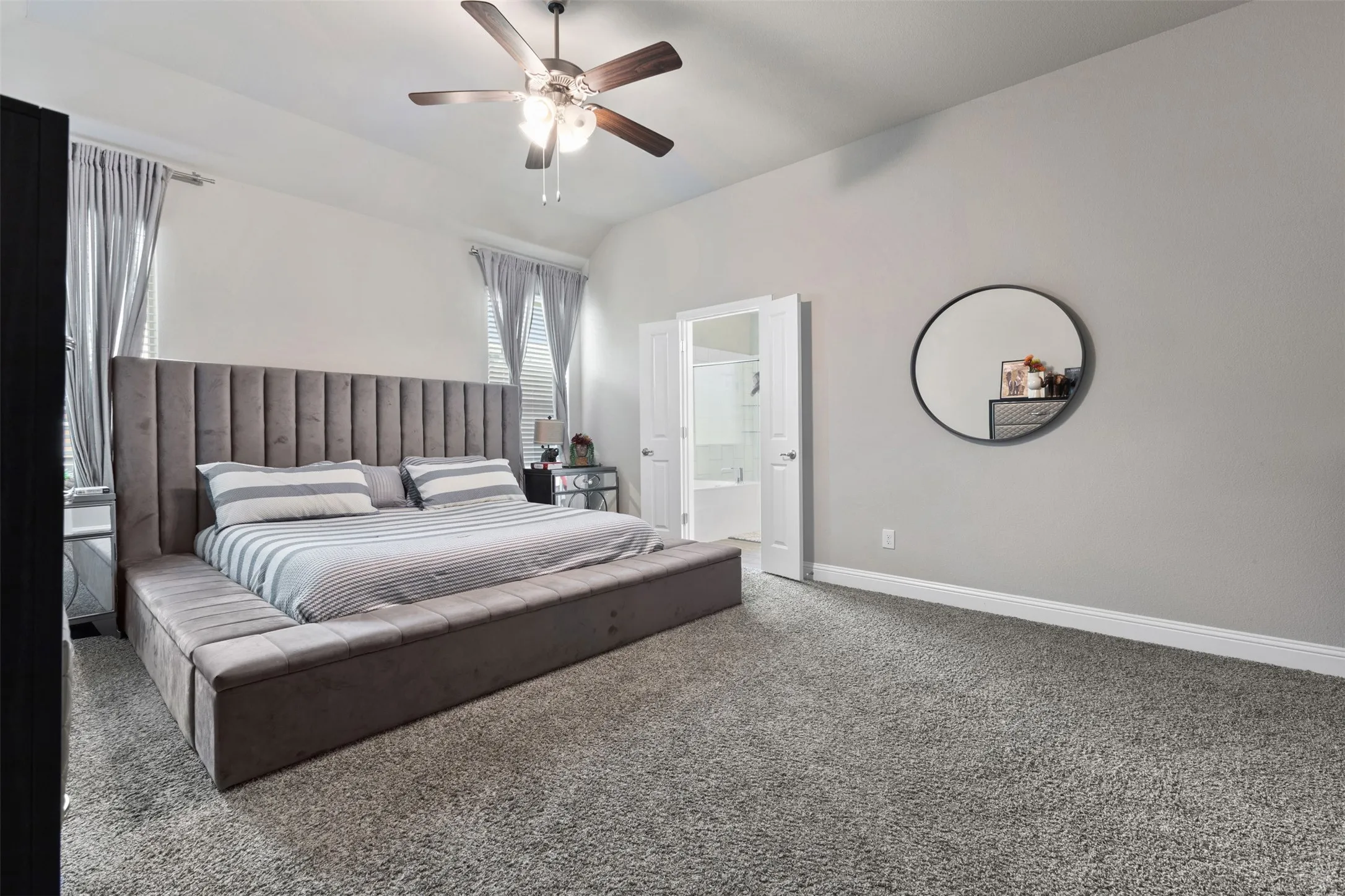 Spacious bedroom featuring plush gray carpeting, neutral wall tones, and a ceiling fan with integrated lighting