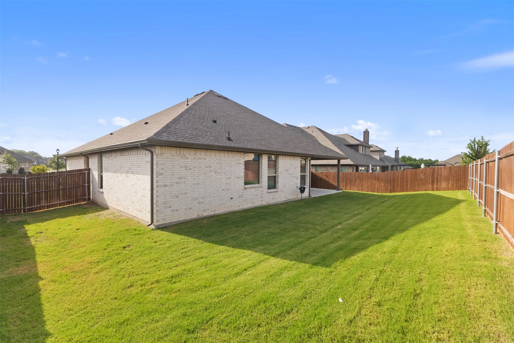 Expansive backyard featuring a manicured lawn, a full wooden privacy fence, and a covered patio area