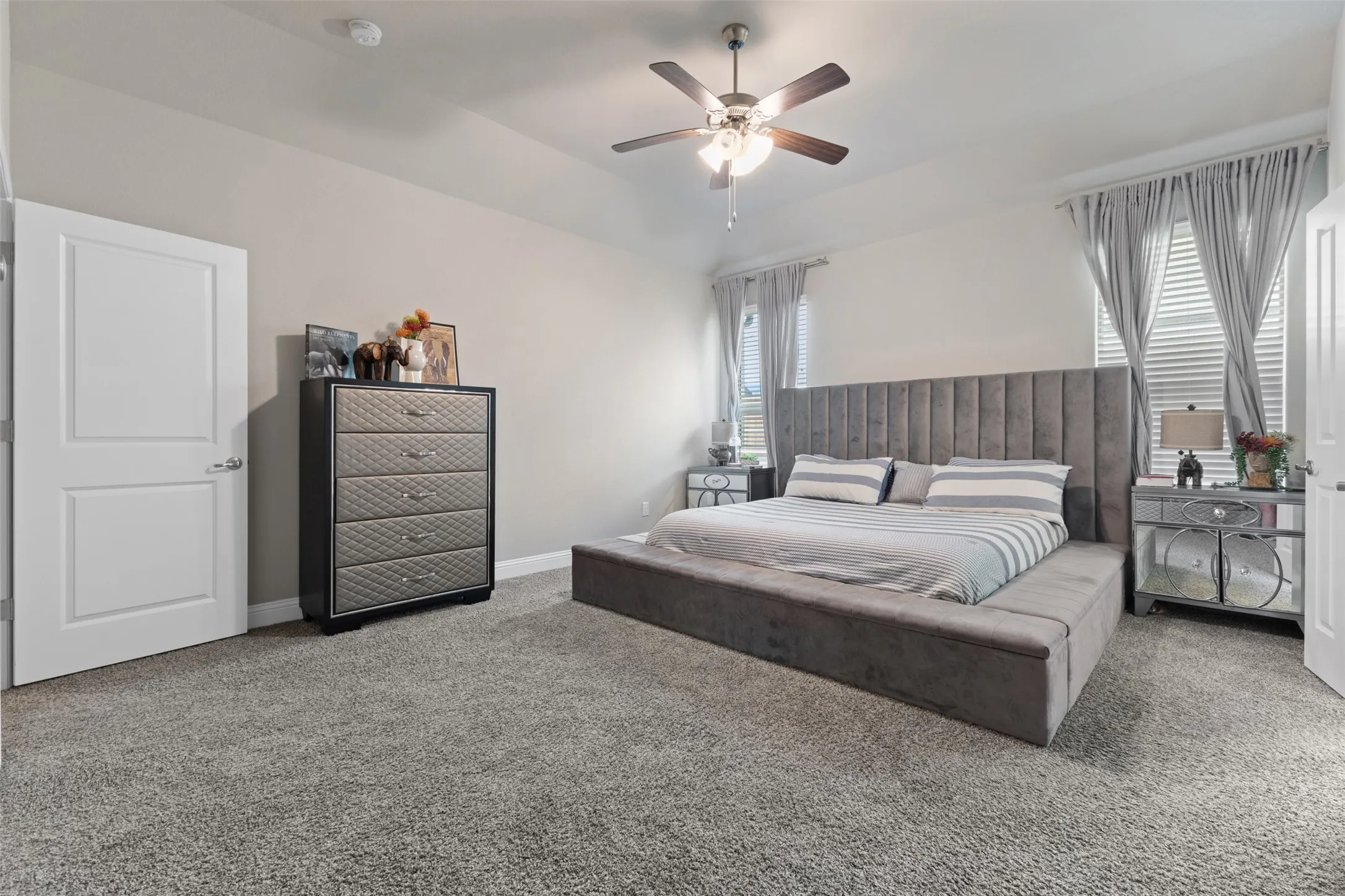 Carpeted bedroom featuring a ceiling fan, recessed lighting, and two oversized windows allowing natural light to flourish